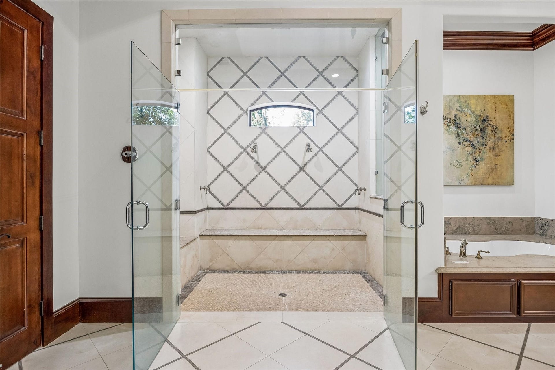 34 Liberty Bell Circle, Bunker Hill Village, TX 77024 The primary bath features an oversized steam shower with frameless glass doors, dual showerheads, a built-in bench, and decorative tile detailing.