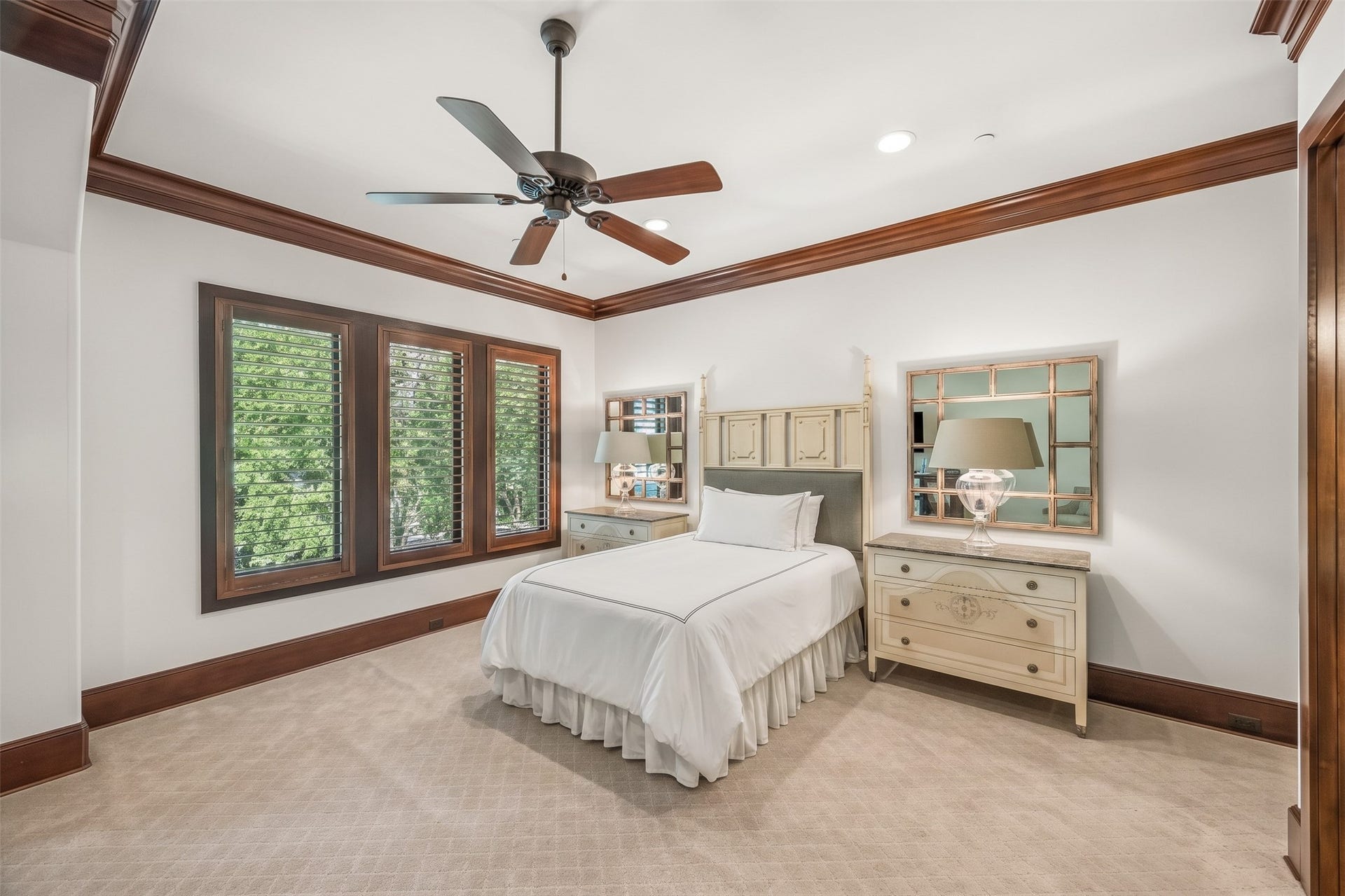 34 Liberty Bell Circle, Bunker Hill Village, TX 77024 This upstairs bedroom offers a spacious layout with neutral carpeting, rich wood trim, and large windows with plantation shutters overlooking the surrounding trees.