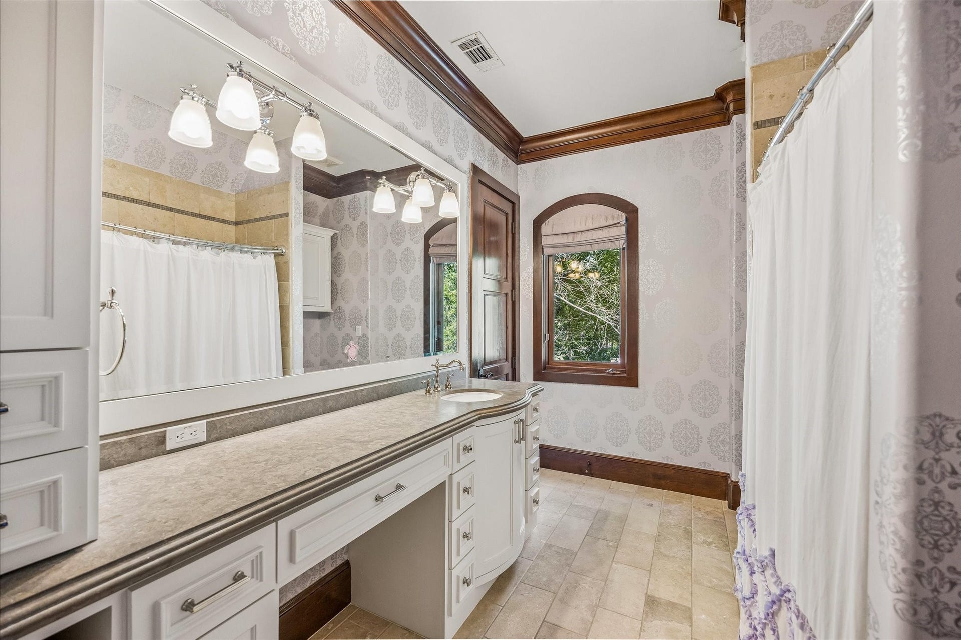 34 Liberty Bell Circle, Bunker Hill Village, TX 77024 The adjoining bathroom offers a spacious vanity with generous counter space, custom cabinetry, a tub and shower combination, and elegant patterned wallcovering.