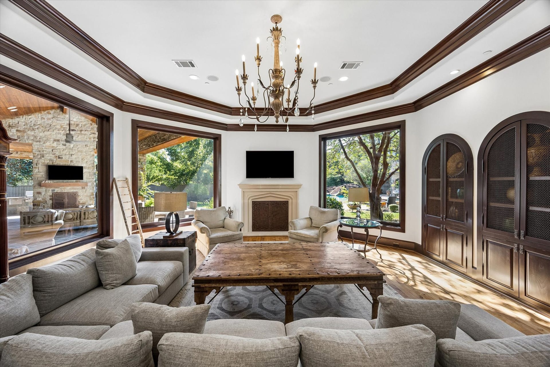 34 Liberty Bell Circle, Bunker Hill Village, TX 77024 Another view of the family room highlights the custom arched cabinetry, detailed ceiling moldings, and expansive windows connecting the interior living space to the covered patio and pool beyond.