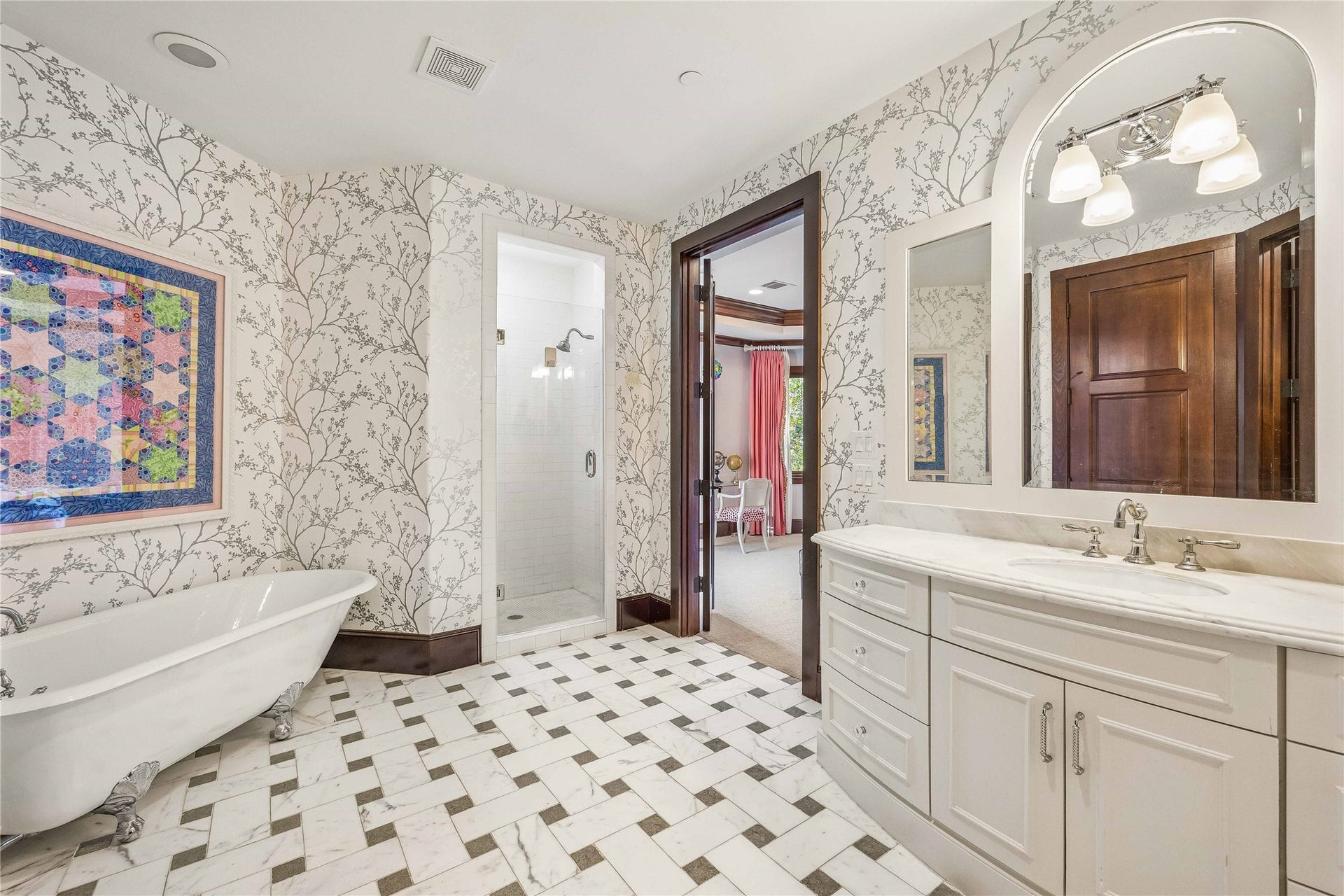34 Liberty Bell Circle, Bunker Hill Village, TX 77024 The adjoining bath features a classic clawfoot soaking tub, separate walk-in shower, marble-patterned tile flooring, and delicate botanical wallcovering.