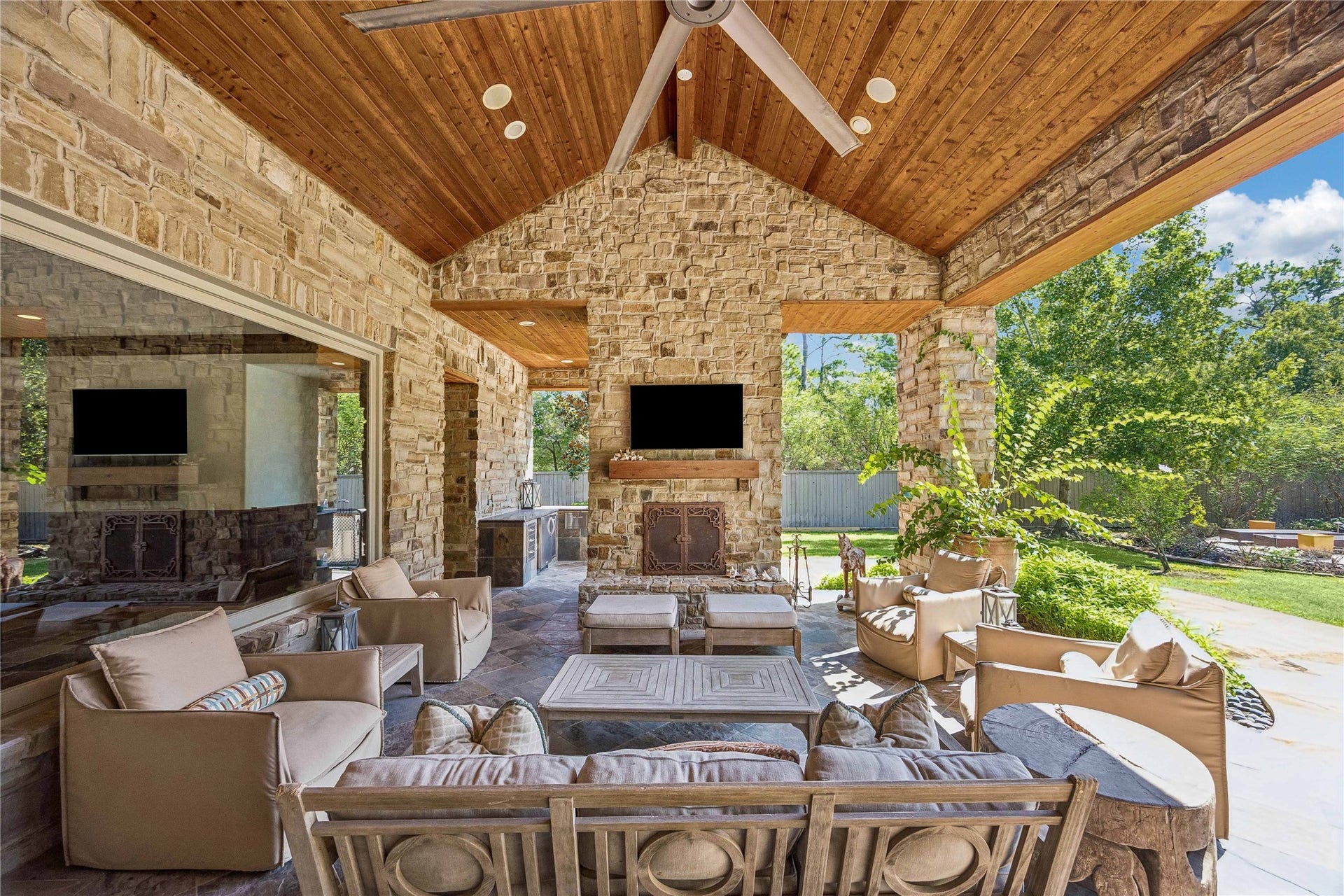 34 Liberty Bell Circle, Bunker Hill Village, TX 77024 Designed for year-round entertaining, the expansive covered patio offers a seamless transition between indoor and outdoor living, with a soaring wood-plank ceiling, stone fireplace, and views of the resort-style pool.