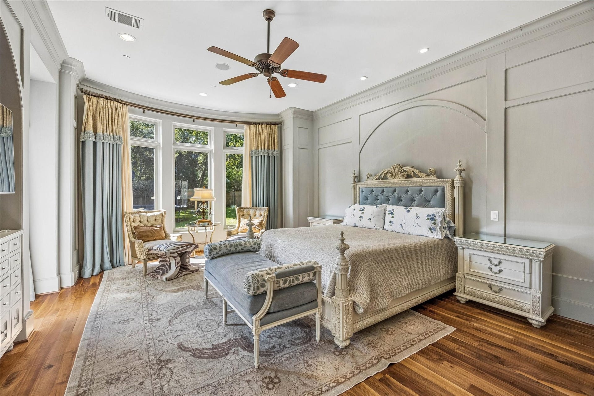34 Liberty Bell Circle, Bunker Hill Village, TX 77024 The first-floor primary suite offers a peaceful retreat with beautiful wall paneling, hardwood floors, a coffee bar, and a curved wall of windows overlooking the backyard.