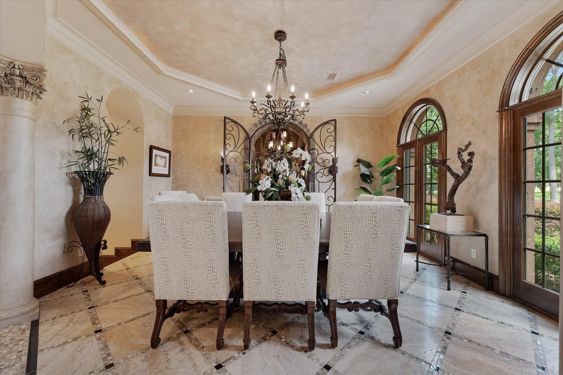 28322 Meadow Forest, Magnolia, TX 77355 The formal dining room boosts arched columns and travertine flooring with a custom tile pattern.
Arched windows overlook the front lawn. Integrate crown molding, recessed speakers, recessed lighting, and a custom chandelier enhance the elegance. The custom tray ceiling with cove lighting and Venetian plastered walls add to the sophisticated ambiance. Custom arched iron gates lead to the wine room, and an arched opening leads to the butler's pantry hallway, providing two different ways to access the kitchen