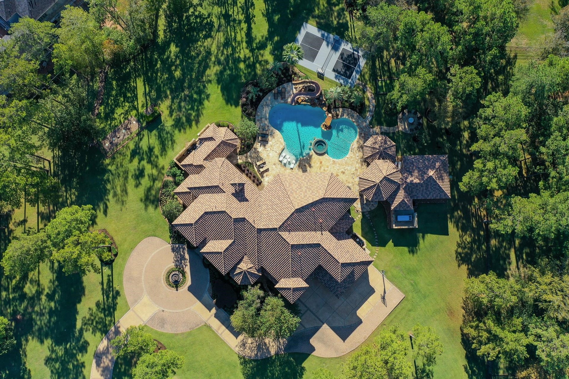 28322 Meadow Forest, Magnolia, TX 77355 The expansive outdoor entertainment area includes a pickleball court, resort-style pool, bocce ball Court, wood burning fire pit with seating area surrounding it ,Summer Kitchen With Granite Countertop, Gas Grill With Side Burner, Sink, and outdoor fridge., entertainment pavilion with a fireplace and seating area that connects to the guest house, glass fire pit table, and a full outdoor bath.