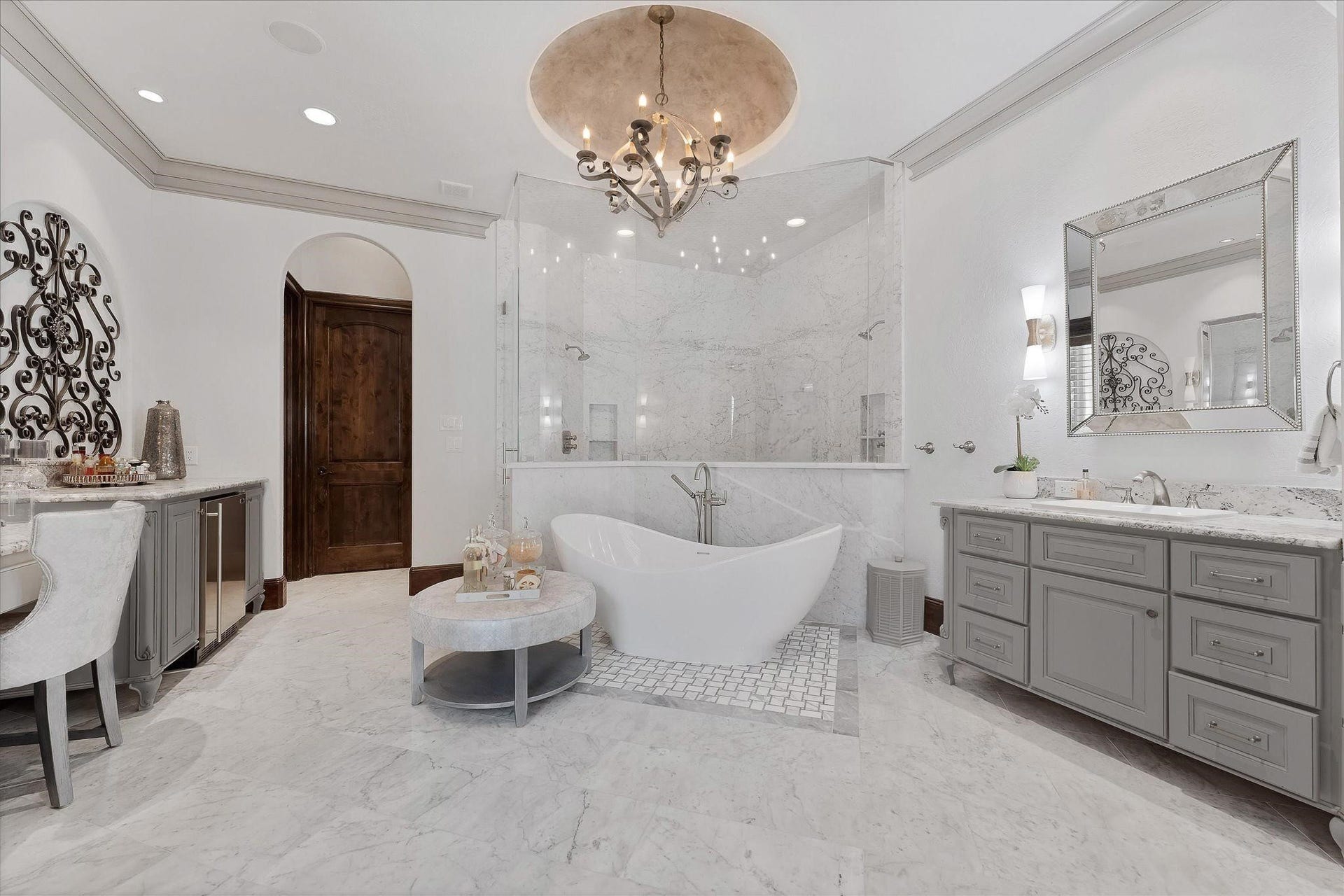 28322 Meadow Forest, Magnolia, TX 77355 Fully renovated Primary ensuite boosting Carrara marble walk-in steam shower with a frameless glass entry door, dual shower heads, designer polished nickel plumbing fixtures, built-in bench seats, and Carrara marble mosaic tile on the floor and ceiling. A freestanding soaking tub surrounded by Intricate tile pattern and Carrara marble flooring. An exterior door with custom wood shutters leads to the backyard and pool area,