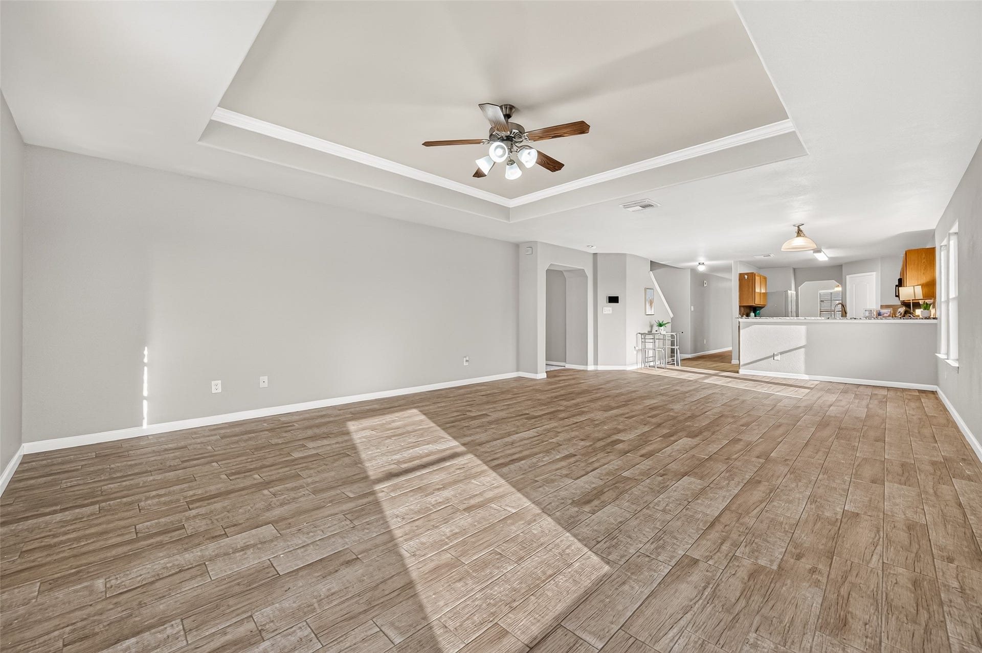 19707 Dayton Springs Drive, Cypress, TX 77429 Spacious living area with wood-look flooring, a stylish tray ceiling, and a seamless flow into the modern kitchen, perfect for entertaining.