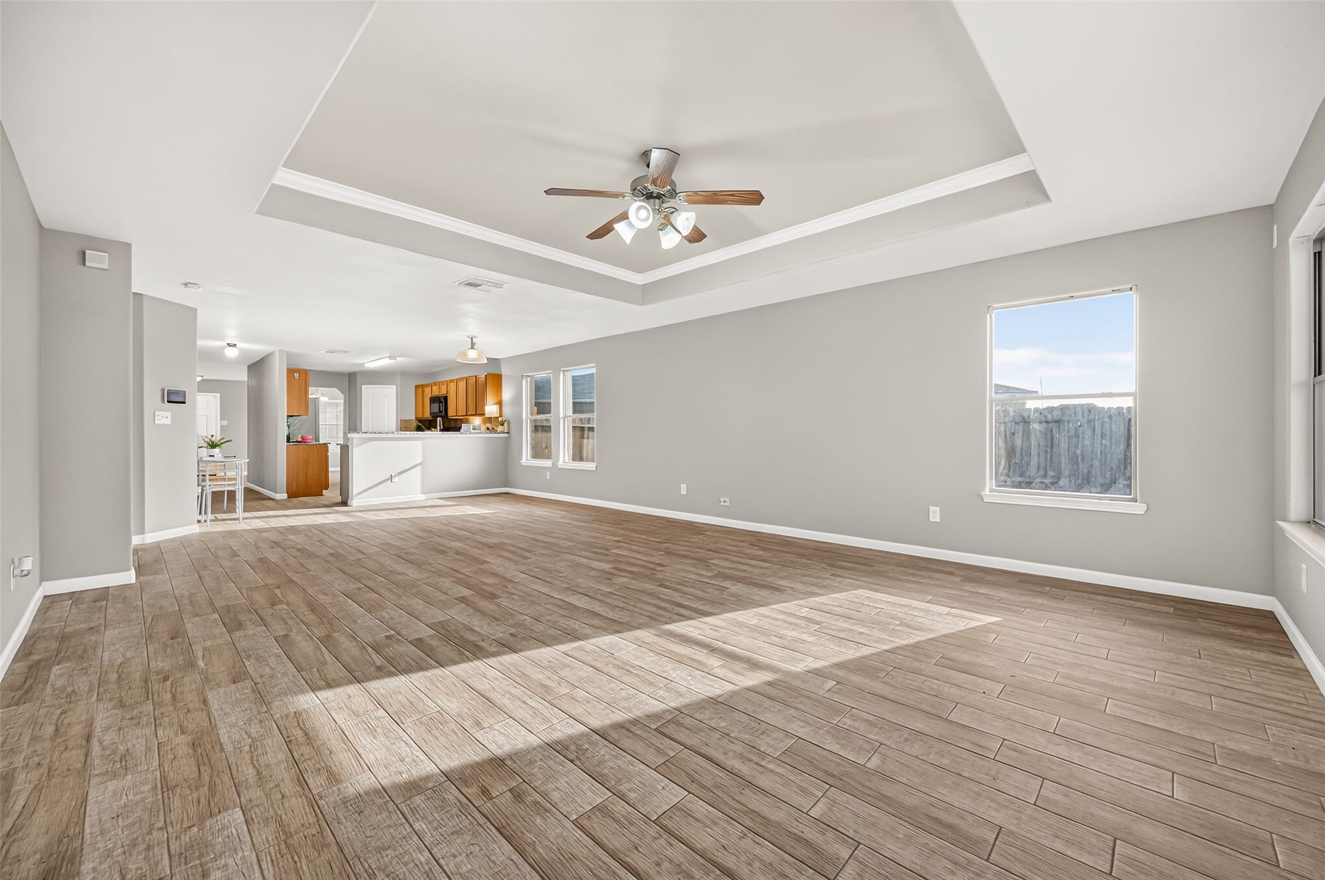 19707 Dayton Springs Drive, Cypress, TX 77429 Spacious open-concept living area with elegant tray ceiling, wood-look tile flooring, and abundant natural light, seamlessly flowing into your kitchen.