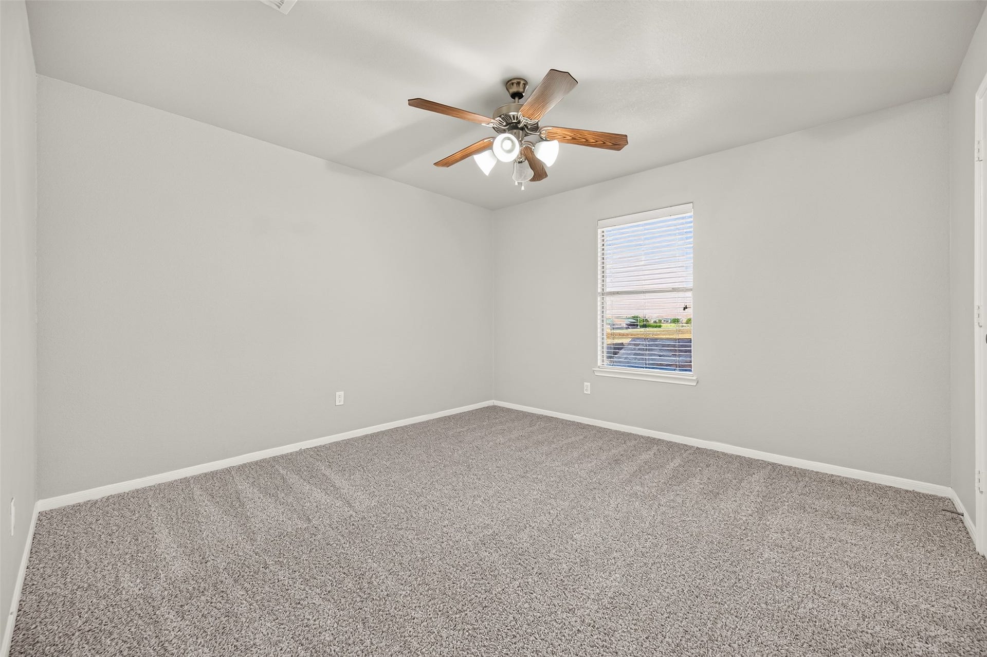 19707 Dayton Springs Drive, Cypress, TX 77429 Spacious bedroom with soft carpeting, neutral gray walls, and a ceiling fan, illuminated by natural light from a large window.