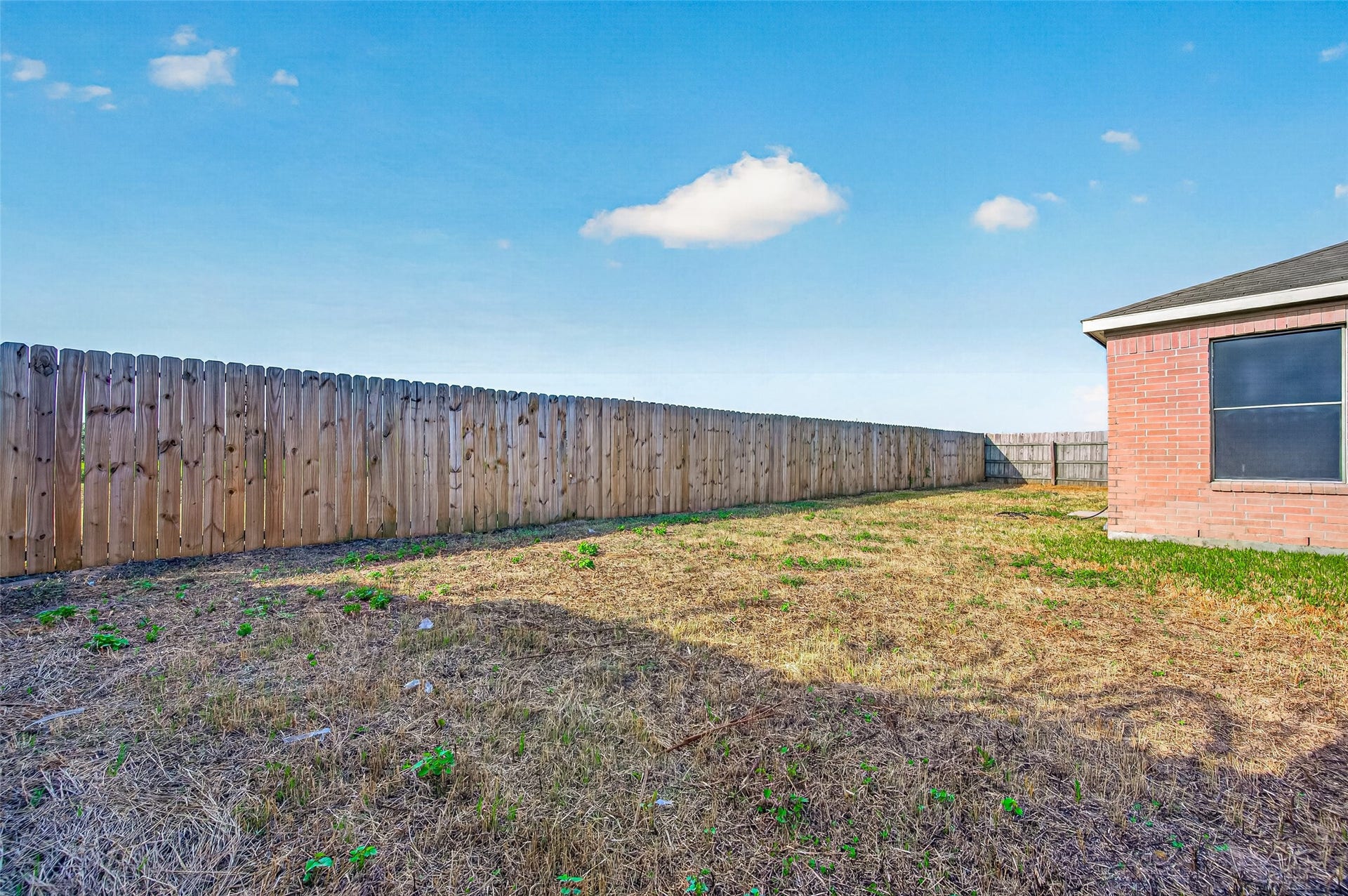 19707 Dayton Springs Drive, Cypress, TX 77429 Spacious fenced backyard with plenty of potential for landscaping or outdoor activities, adjacent to a brick exterior.
