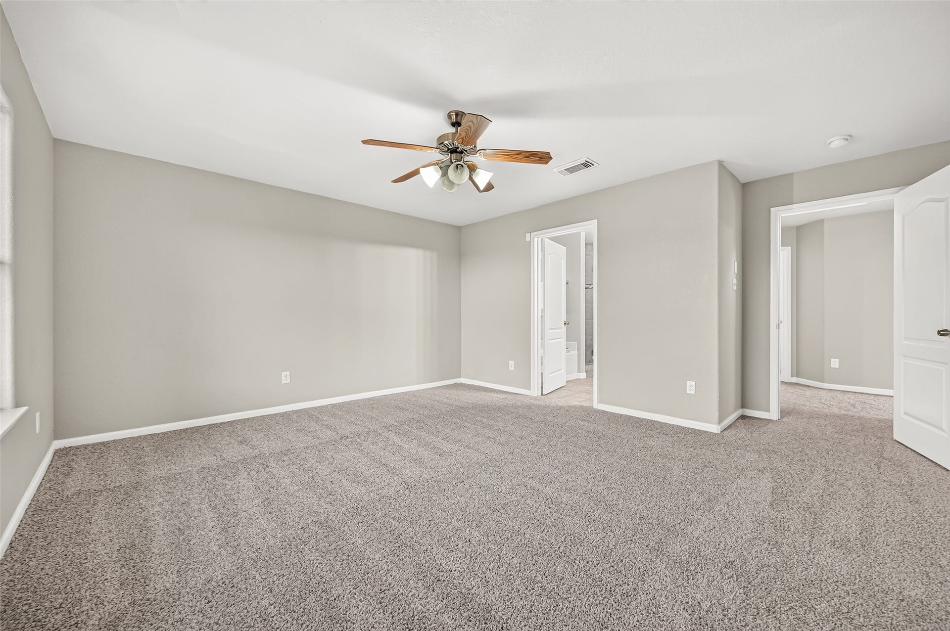 19707 Dayton Springs Drive, Cypress, TX 77429 Spacious bedroom with plush new carpeting, neutral walls, and a ceiling fan, leading to an ensuite bathroom for added convenience.