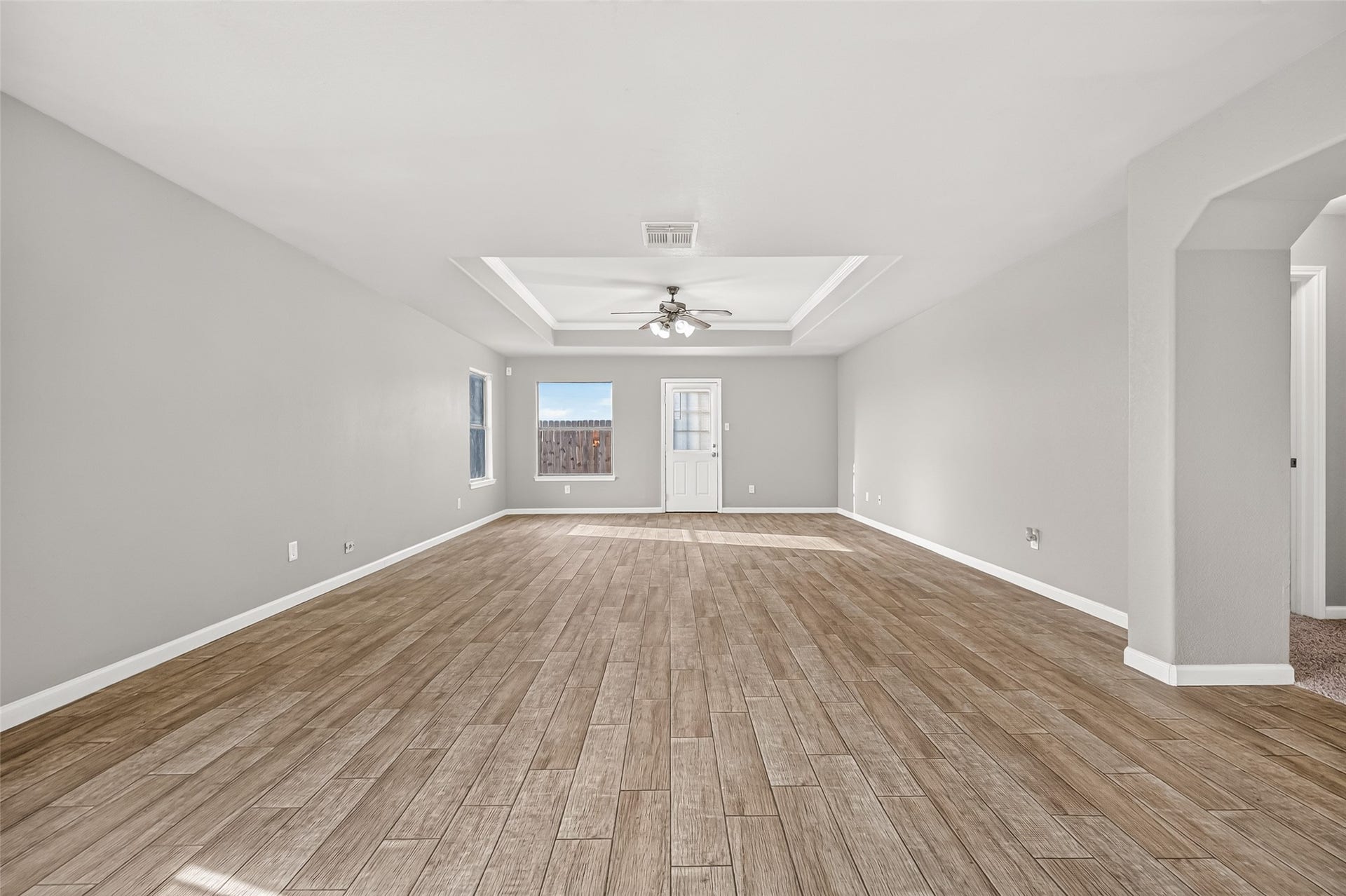 19707 Dayton Springs Drive, Cypress, TX 77429 Spacious living area with wood-look tile flooring, neutral gray walls, and a stylish tray ceiling featuring a modern ceiling fan. Natural light pours in through multiple windows, complementing the open and airy feel.