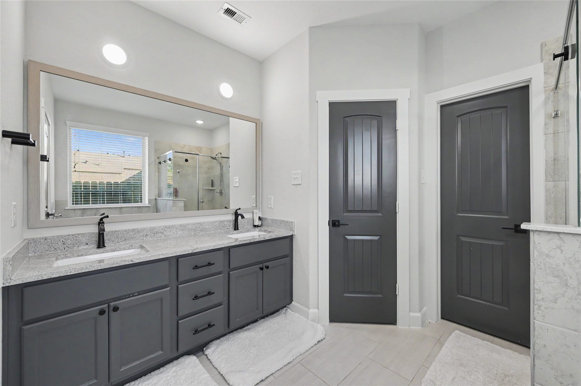 The beautifully designed primary bathroom features a spacious dual-sink vanity with ample cabinetry and a separate glass-enclosed shower. Modern finishes, generous counter space, and a thoughtfully arranged layout provide both comfort and everyday convenience.