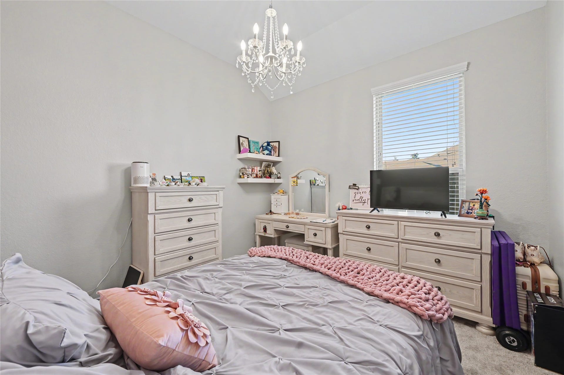 This charming bedroom features beautiful natural light, a decorative chandelier, and a comfortable layout with room for furnishings. The bright walls and inviting atmosphere create a lovely space for rest and relaxation.