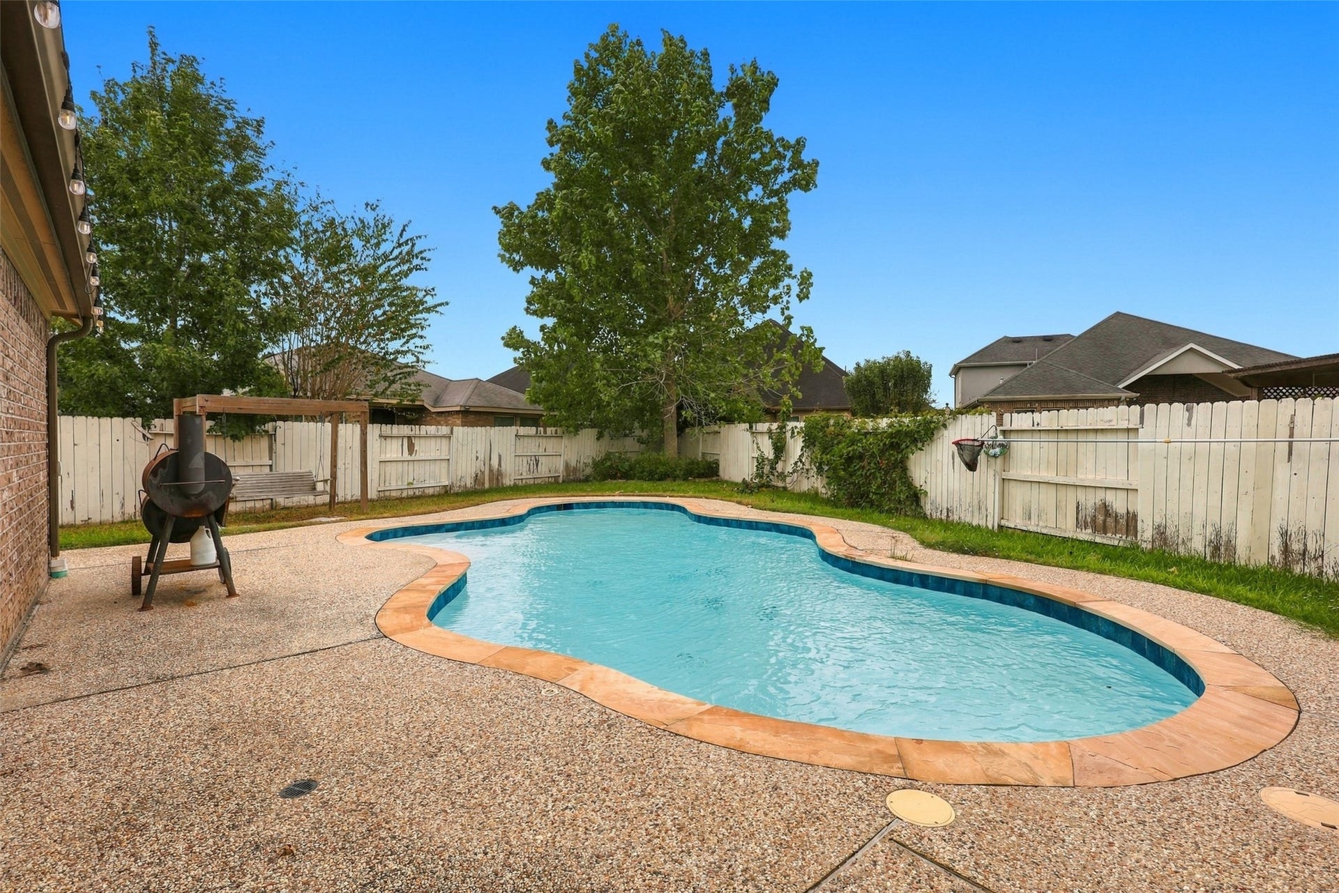 326 Lake Rim Drive, Rosenberg, TX 77469 Backyard pool surrounded by a textured deck, with mature trees and a nearby swing.