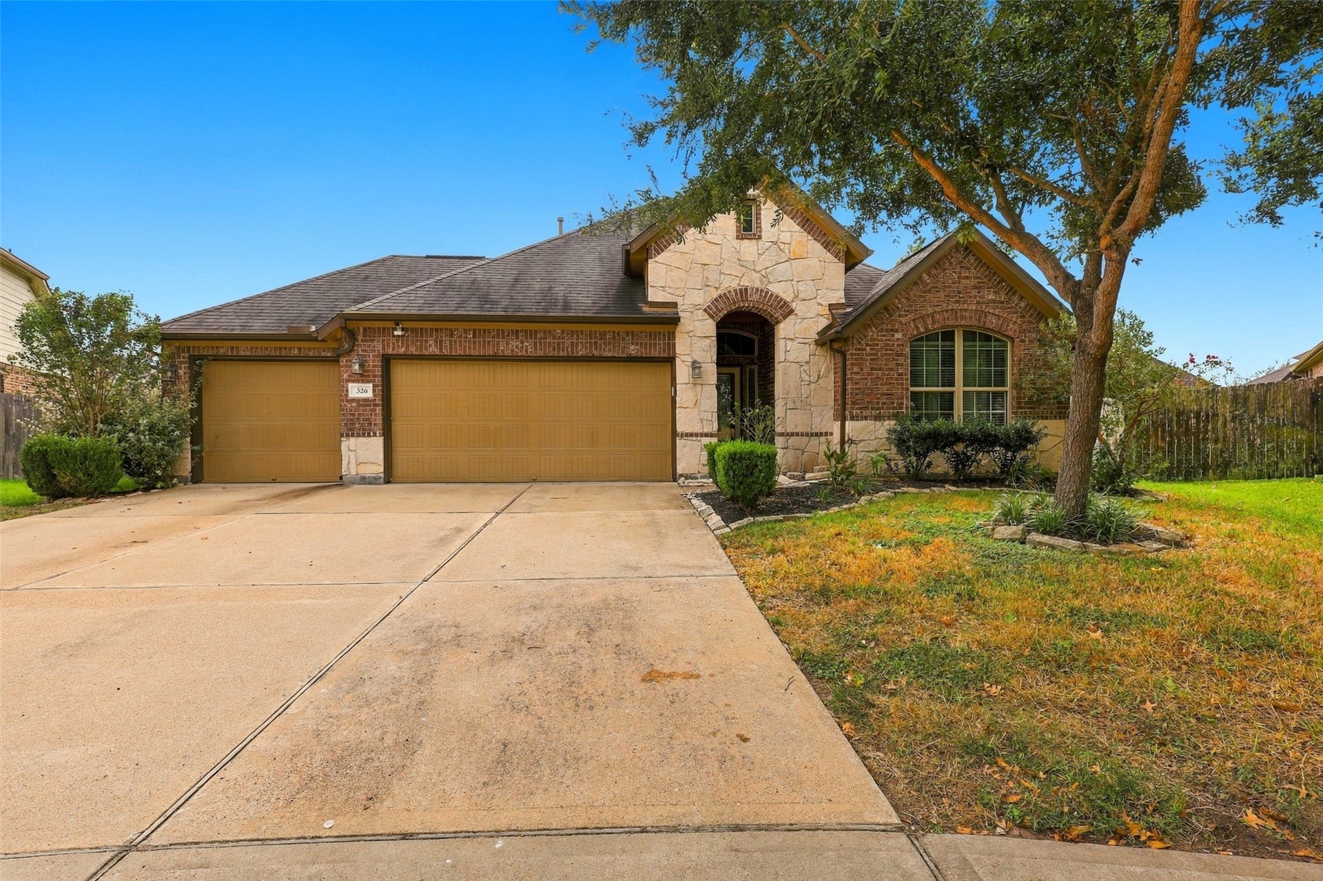 326 Lake Rim Drive, Rosenberg, TX 77469 Brick and stone exterior with a three-car garage, wide driveway, and mature shade tree.