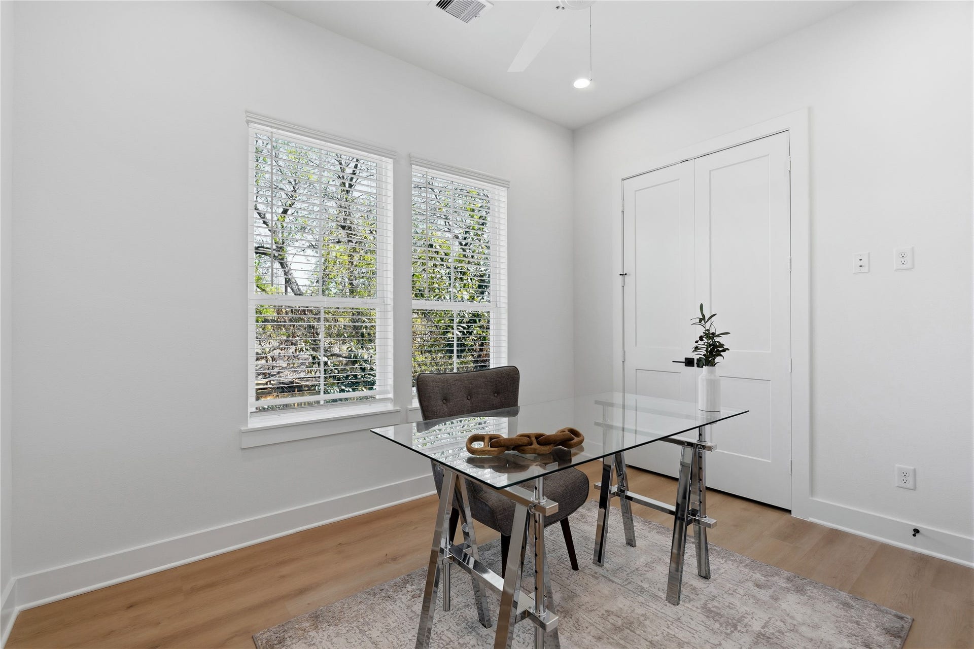 Dual double-hung windows provide ample natural light to this crisp, white-walled workspace. Continuous wide-plank flooring and high ceilings maintain the home's airy architectural theme.