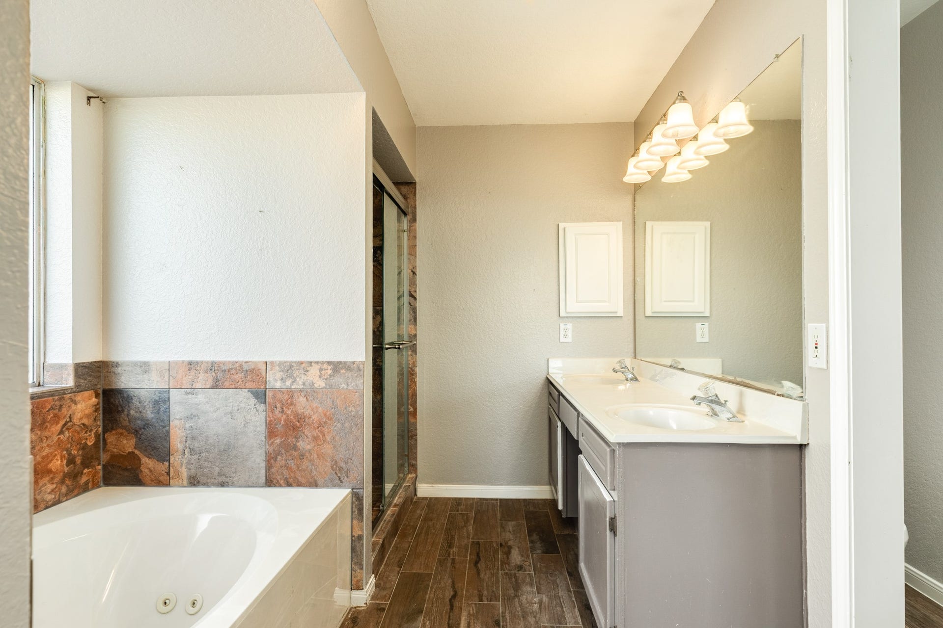 3425 Van Ness Drive, Alvin, TX 77511 Spacious primary bathroom featuring a luxurious jetted tub, dual sinks, sleek tile flooring, and a large mirror with elegant lighting.