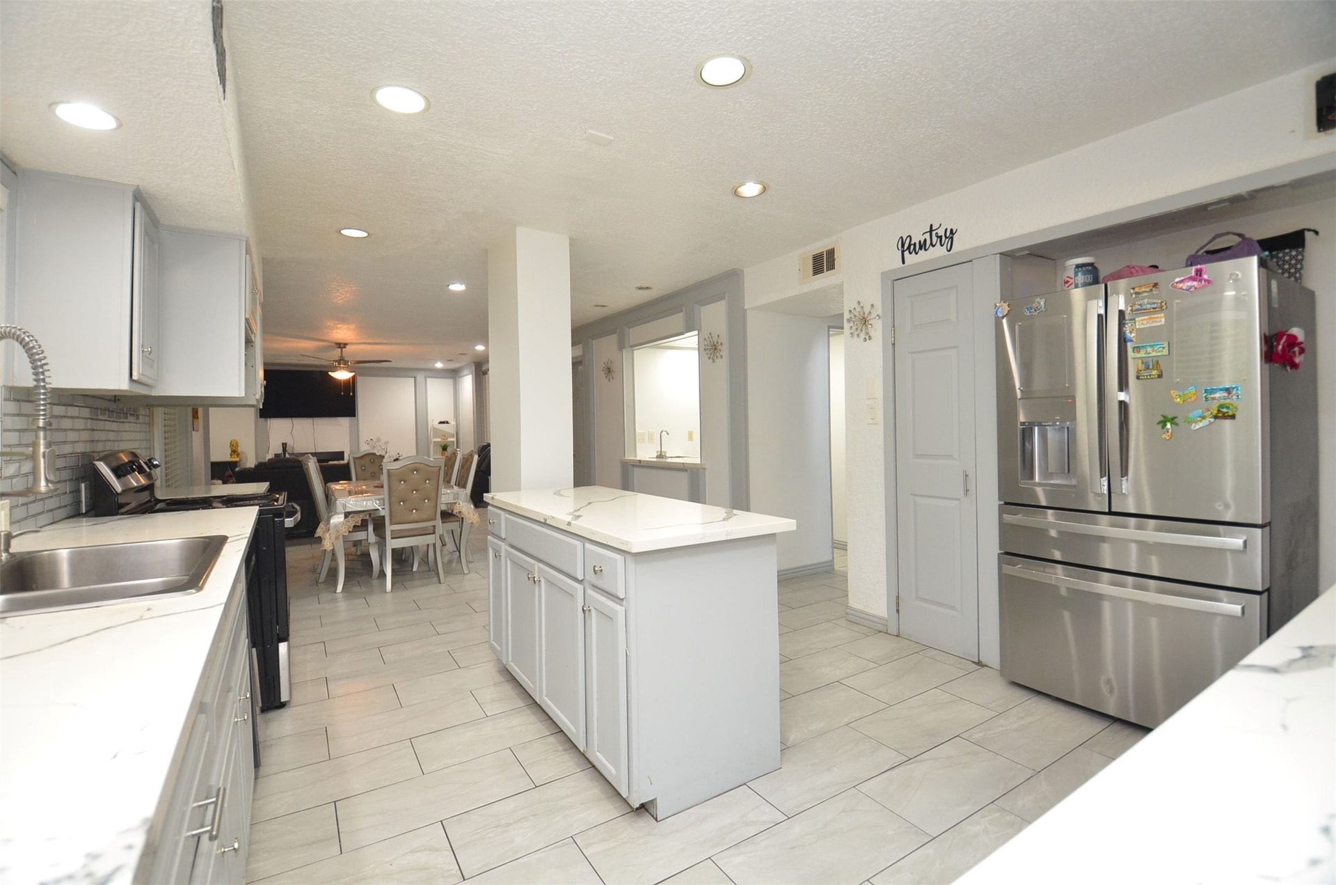 17821 S Cypress Villas Drive, Spring, TX 77379 Open-concept kitchen with center island featuring stylish modern quartz tops, painted gray cabinetry, pantry closet, stainless-steel refrigerator, recessed lighting and light tile flooring, flowing seamlessly to the dining and living areas.