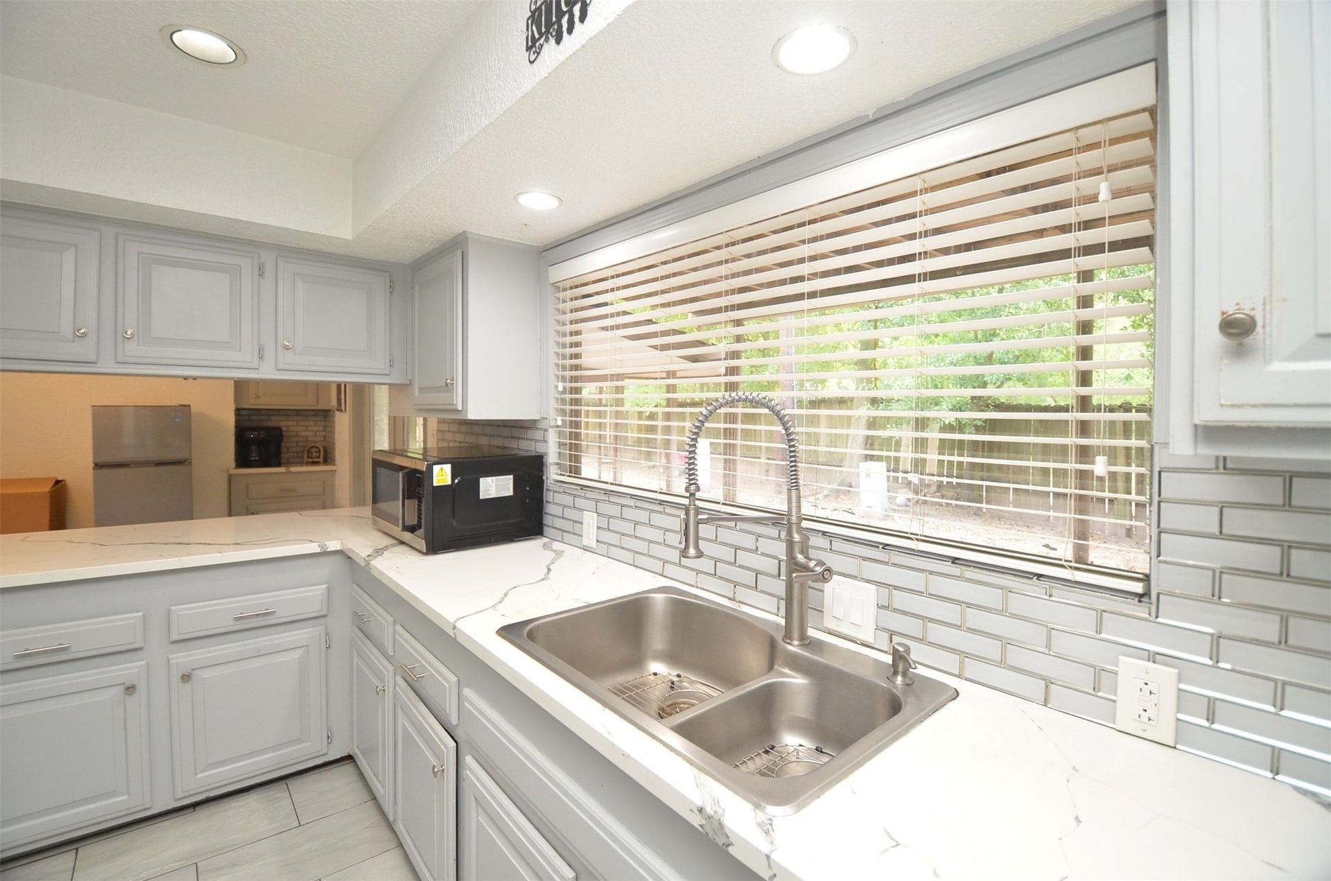 17821 S Cypress Villas Drive, Spring, TX 77379 New open-concept kitchen with stylish modern quartz counters, painted gray cabinetry, subway-tile backsplash, stainless double sink with gooseneck faucet, recessed lighting, and large window overlooking the backyard.