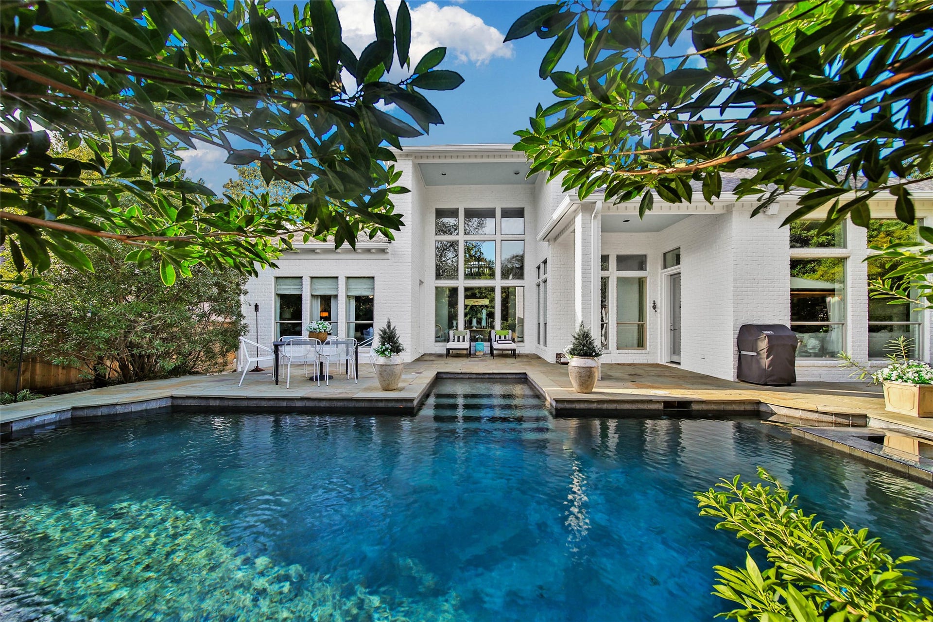 39 W Old Sterling Circle, The Woodlands, TX 77382 Classic home with a luxurious pool, patio, and abundant natural light from large windows, all surrounded by lush greenery.