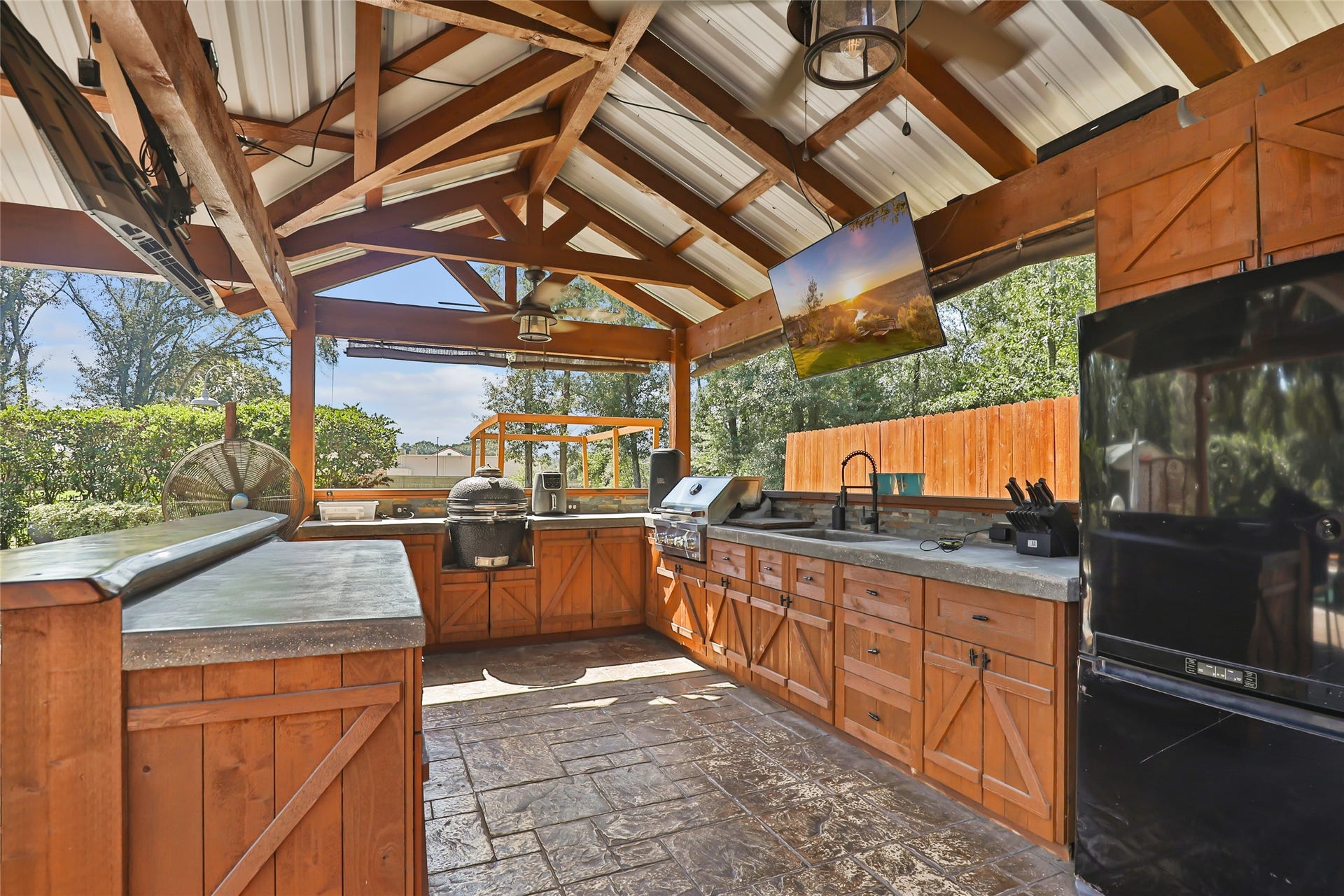 25107 Goodson Road, Splendora, TX 77372 Experience outdoor living at its finest with this spacious, fully-equipped kitchen featuring a built-in grill, ample counter space, and modern appliances, all under a charming vaulted ceiling.