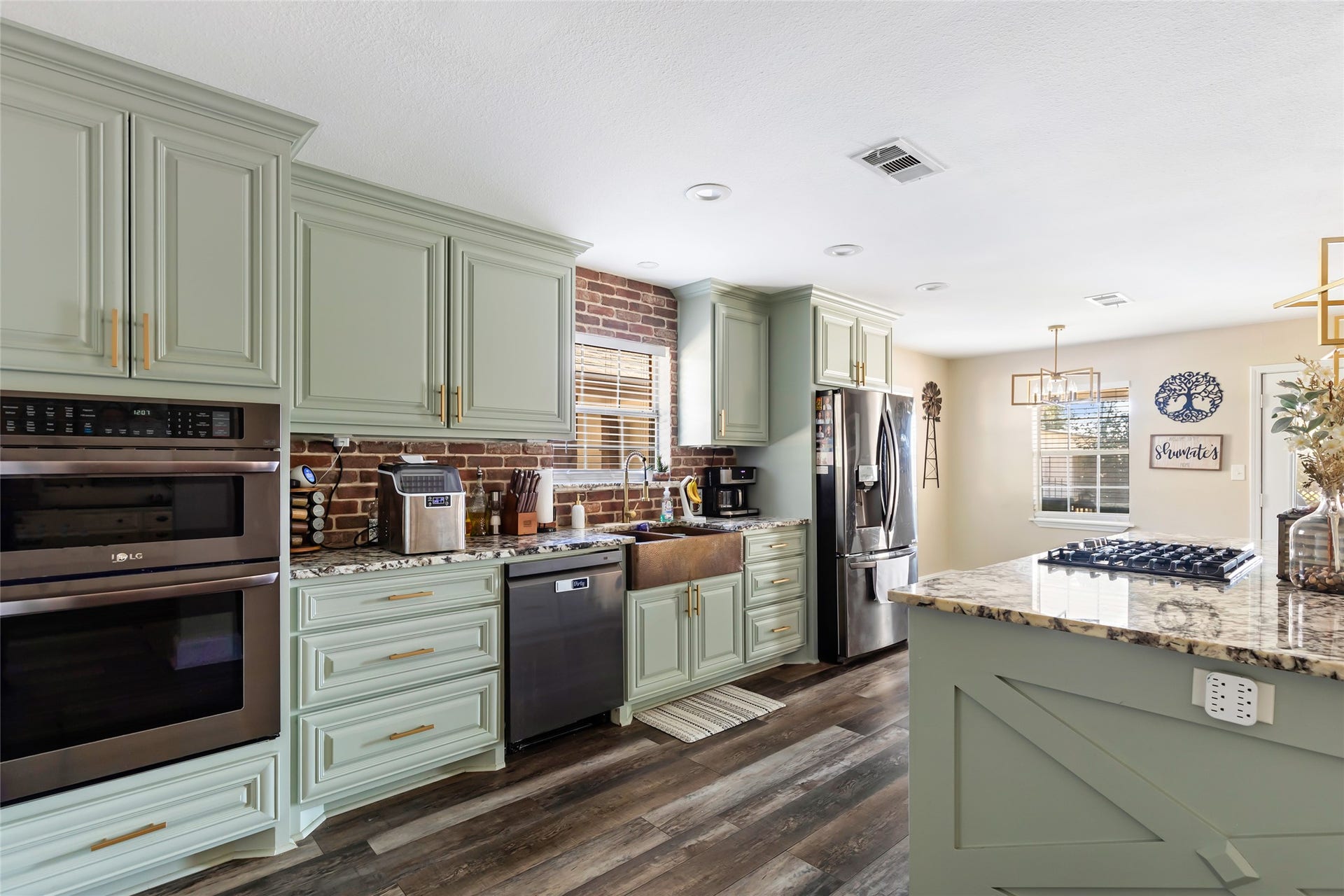 25107 Goodson Road, Splendora, TX 77372 Charming kitchen with sage green cabinetry and a warm brick backsplash, featuring modern stainless steel appliances and a spacious granite island with a built-in cooktop.