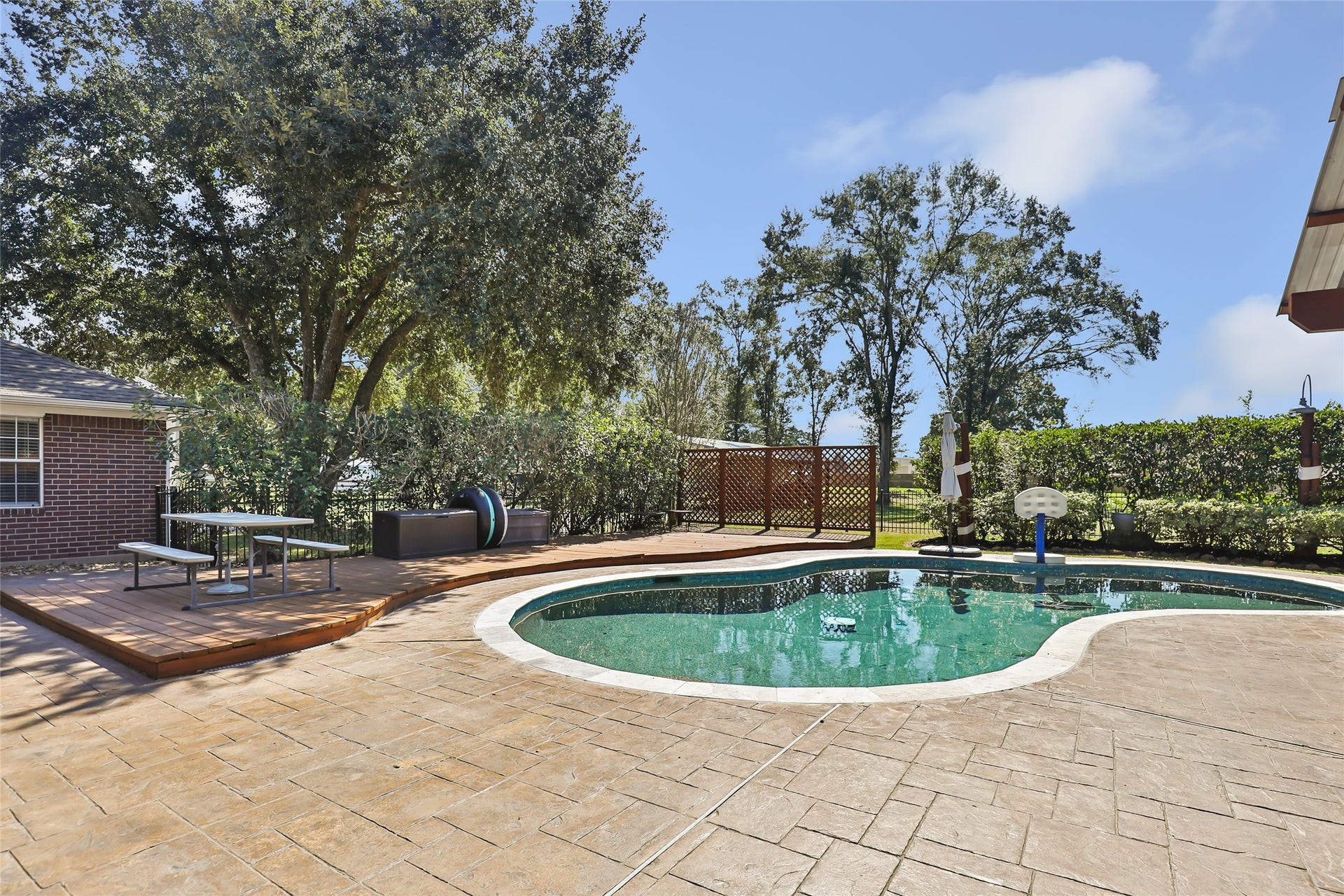 25107 Goodson Road, Splendora, TX 77372 A spacious backyard oasis featuring a sparkling pool with surrounding patio space, shaded by mature trees and complemented by a cozy seating area on a raised deck.