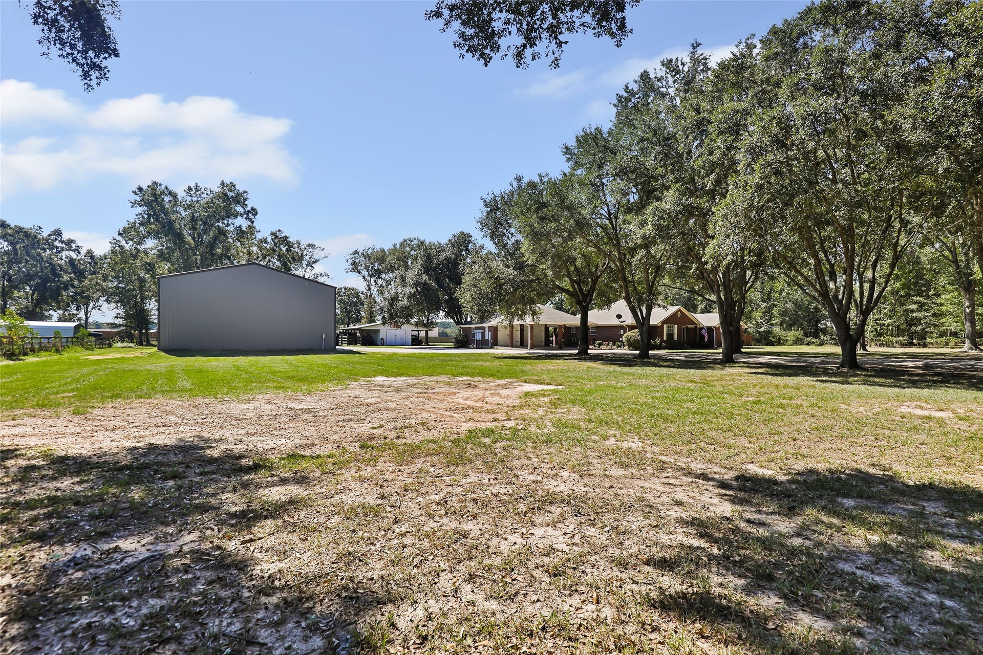 25107 Goodson Road, Splendora, TX 77372 Expansive property with a spacious metal outbuilding and a charming home nestled among mature trees, offering ample outdoor space and privacy.