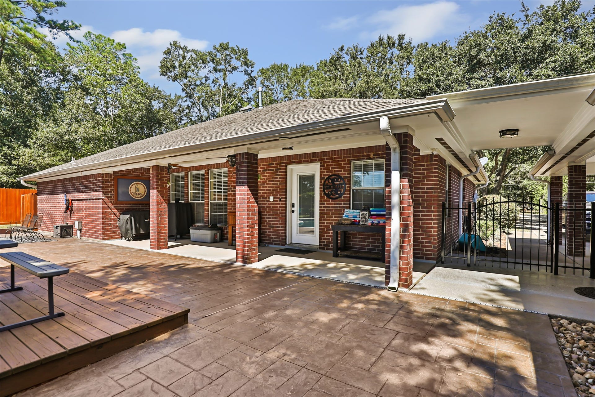 25107 Goodson Road, Splendora, TX 77372 Charming brick home featuring a spacious stamped concrete patio, ideal for outdoor entertaining, surrounded by lush greenery and mature trees.