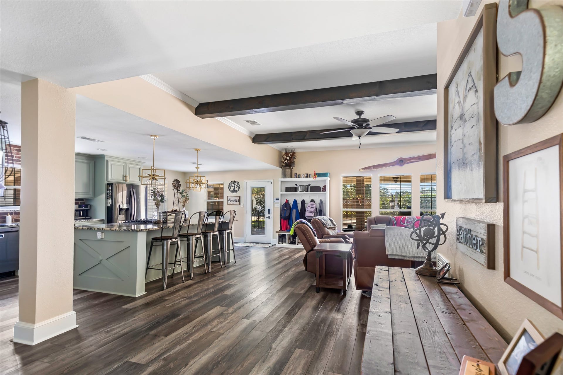 25107 Goodson Road, Splendora, TX 77372 Spacious open floor plan with rustic beams, elegant hardwood floors, and a modern kitchen featuring a large island with seating. Cozy living area with abundant natural light from large windows.