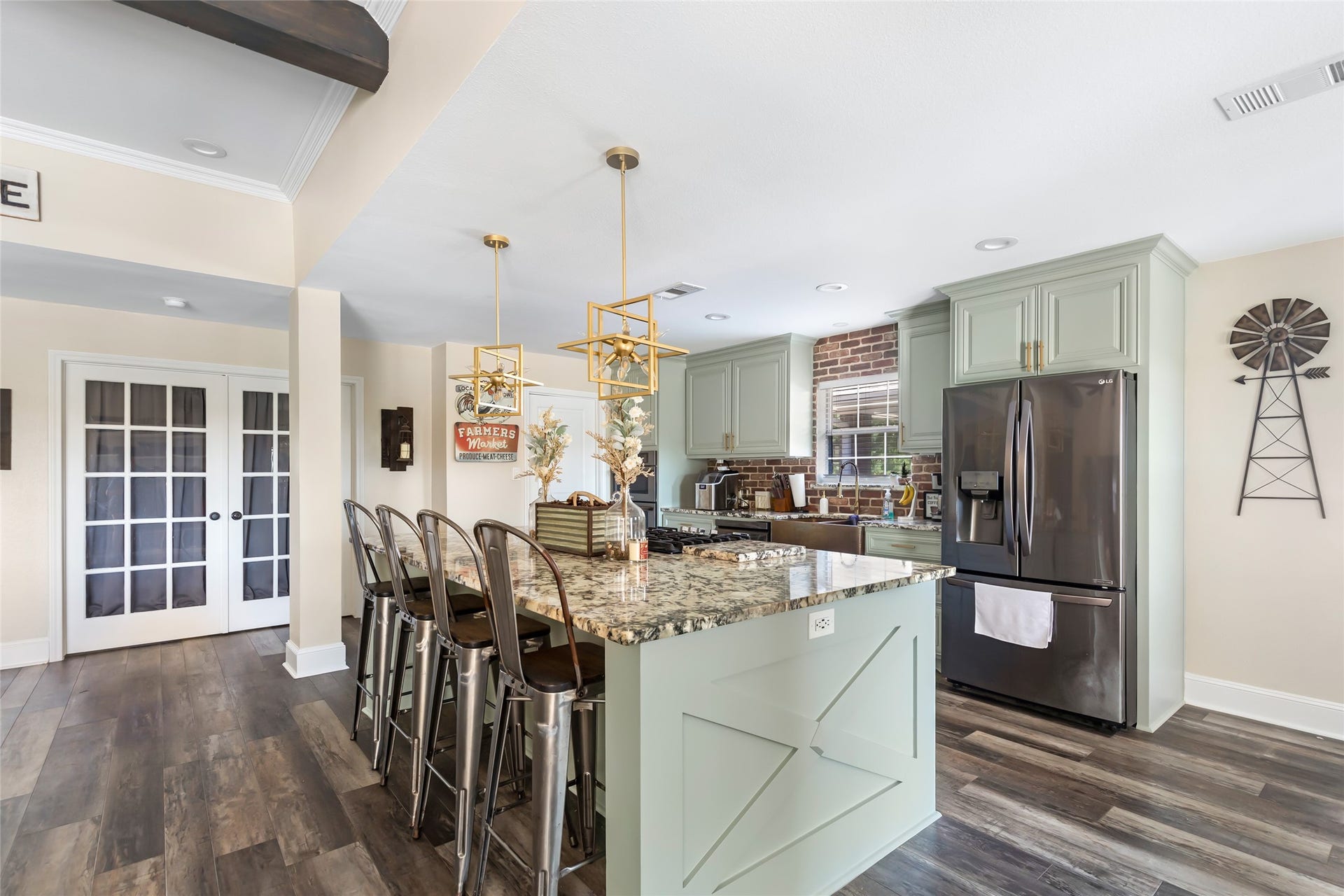 25107 Goodson Road, Splendora, TX 77372 Stylish kitchen featuring a large granite island with seating, modern appliances, and chic pendant lighting, complemented by mint green cabinetry and rustic brick accents.