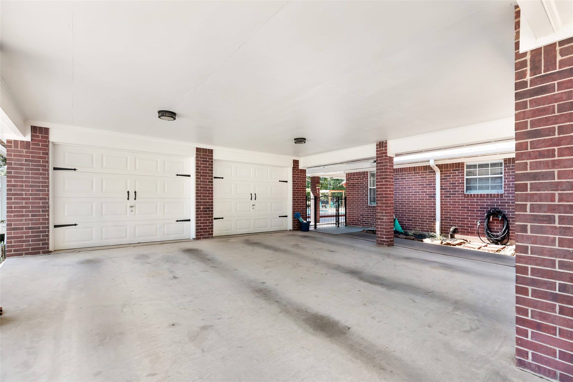 25107 Goodson Road, Splendora, TX 77372 Spacious covered carport with direct access to a three-car garage, featuring elegant brickwork and ample room for additional storage or outdoor activities.