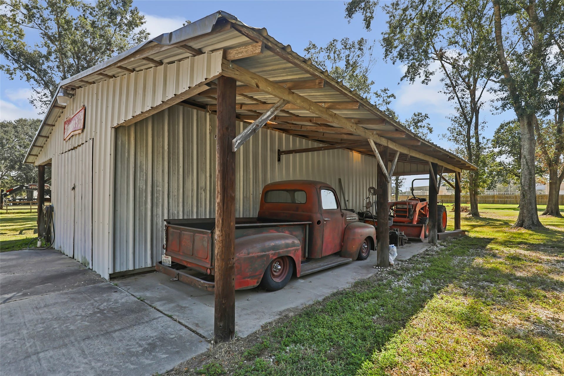 25107 Goodson Road, Splendora, TX 77372 A rustic metal carport with vintage vehicles offers ample storage space, surrounded by mature trees and lush greenery.
