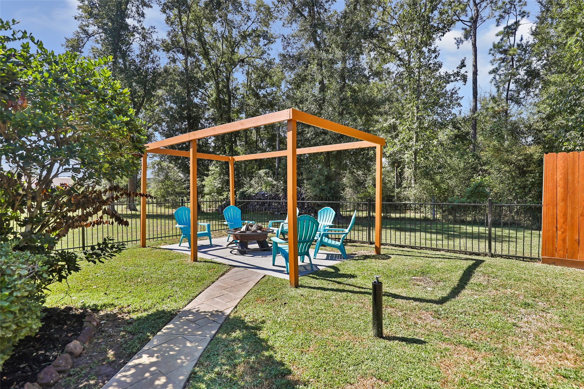 25107 Goodson Road, Splendora, TX 77372 Charming backyard retreat featuring a cozy pergola with vibrant Adirondack chairs surrounding a fire pit, perfect for relaxation and entertaining.