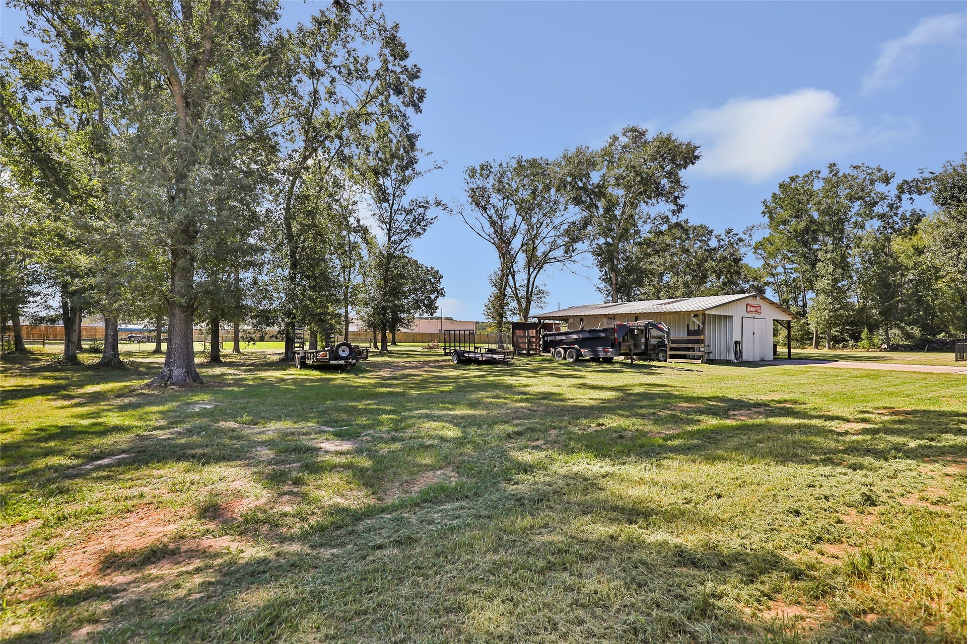 25107 Goodson Road, Splendora, TX 77372 Expansive grassy lot with mature trees, featuring a spacious utility building ideal for storage or projects, offering ample outdoor space and versatility.