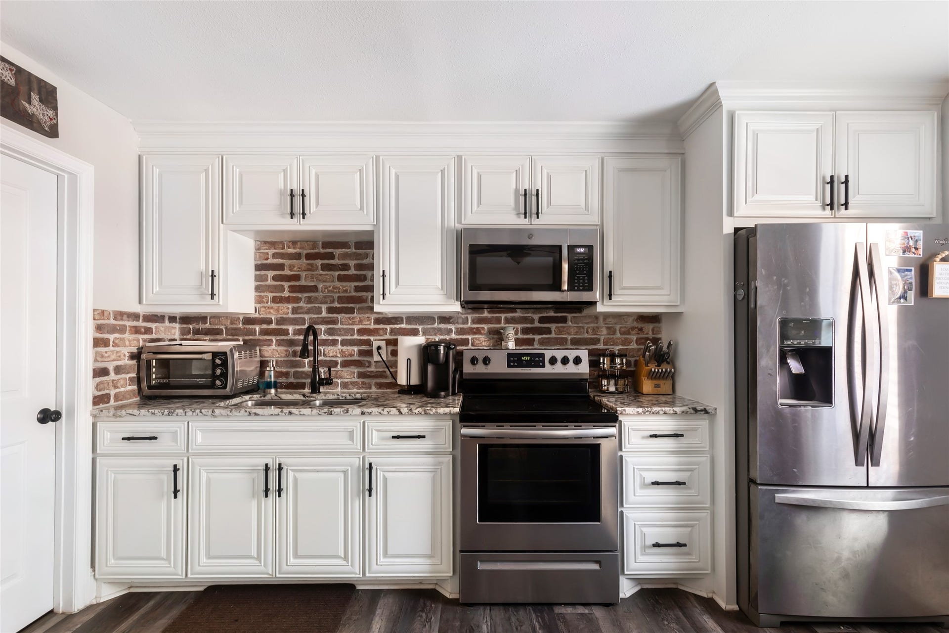 25107 Goodson Road, Splendora, TX 77372 Modern kitchen with sleek stainless steel appliances, elegant white cabinetry, and a stylish brick backsplash.