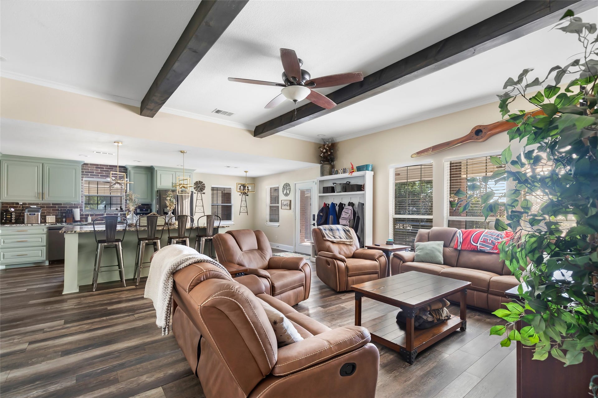 25107 Goodson Road, Splendora, TX 77372 Spacious open-concept living area featuring cozy recliners, elegant wood beam accents, and a seamless flow into a modern kitchen with mint cabinetry and stylish bar seating.