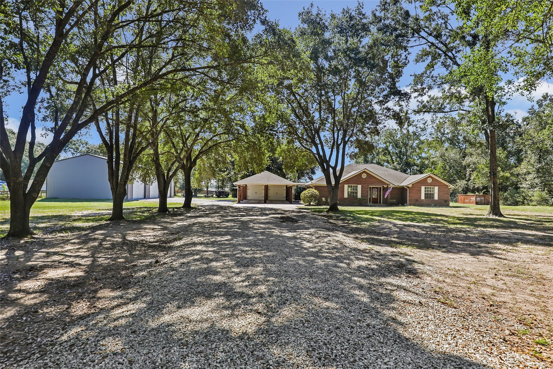 25107 Goodson Road, Splendora, TX 77372 Charming ranch-style home set amid mature trees, offering a spacious front yard with a gravel driveway leading to a detached garage.