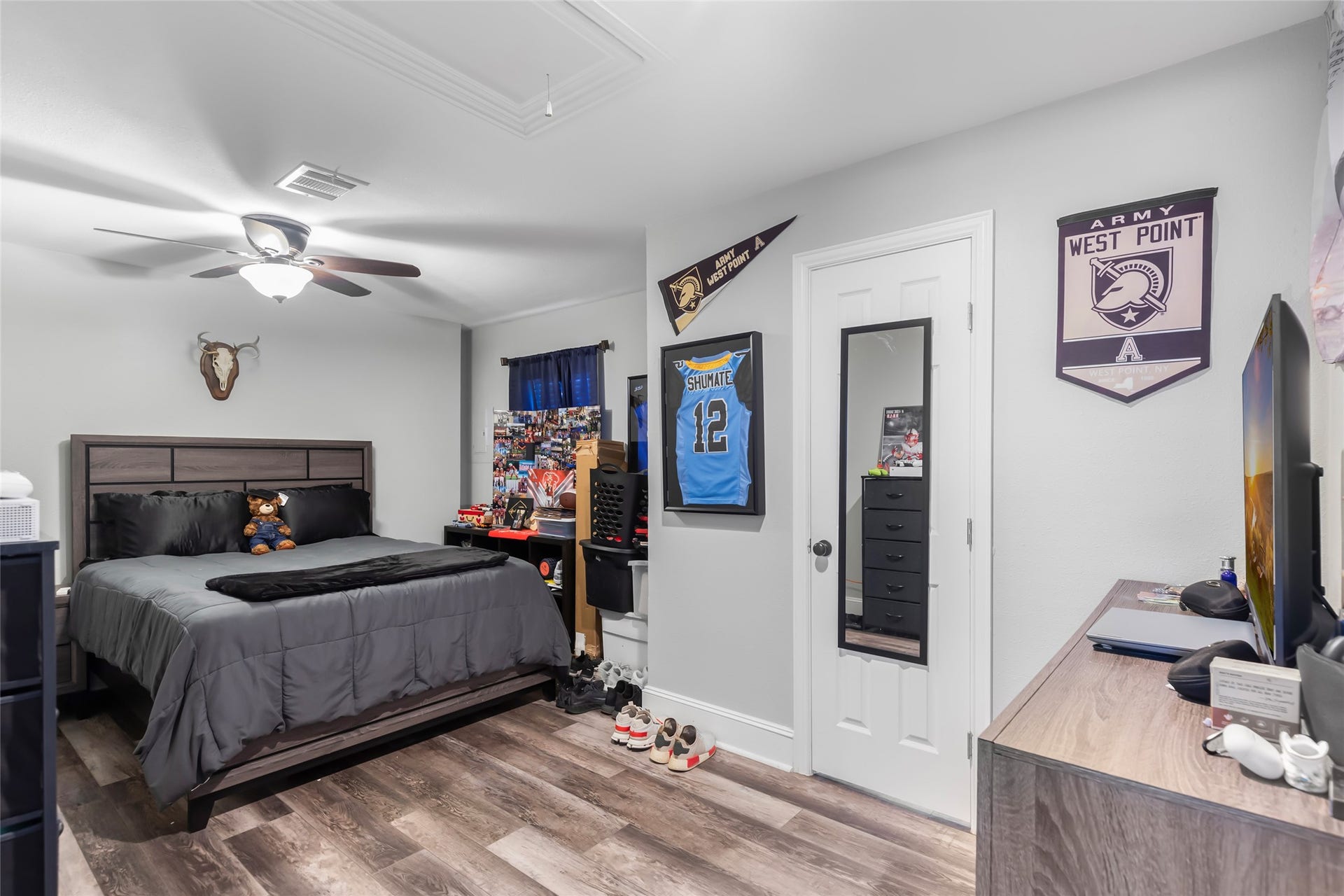 25107 Goodson Road, Splendora, TX 77372 Cozy bedroom featuring sleek hardwood floors, a modern ceiling fan, and ample natural light. Decorated with personal memorabilia, it offers a comfortable space for relaxation and personalization.