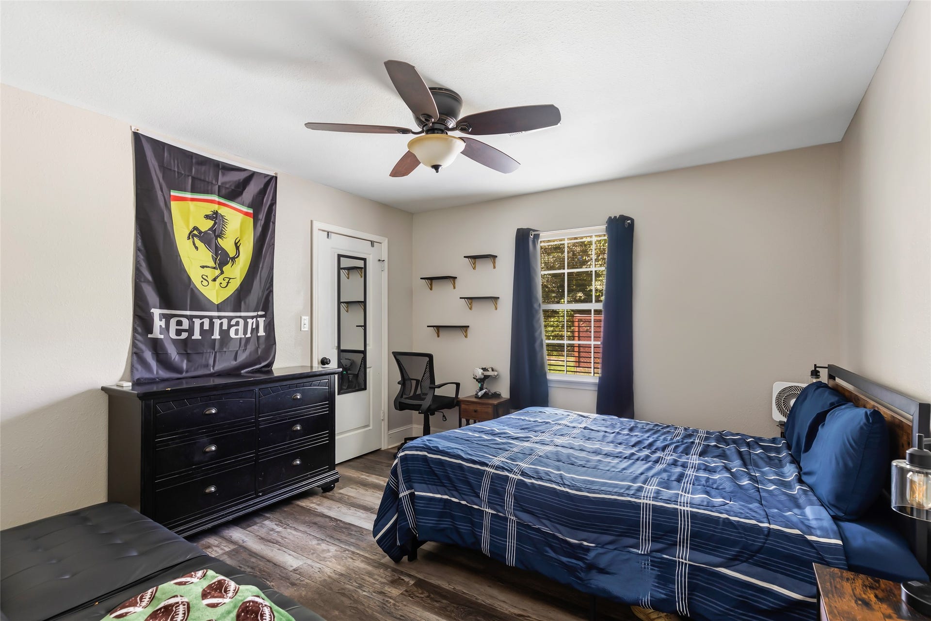 25107 Goodson Road, Splendora, TX 77372 Bright and inviting bedroom with a large window, modern ceiling fan, and stylish wood flooring. Features a cozy bed, ample dresser storage, and tasteful decor.