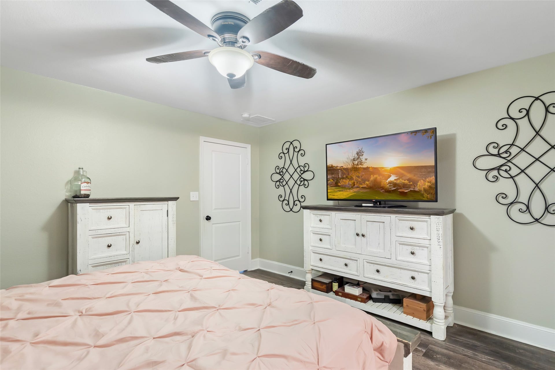 25107 Goodson Road, Splendora, TX 77372 Cozy bedroom with soft green walls features elegant white furniture, a ceiling fan, and a mounted flat-screen TV for modern comfort.