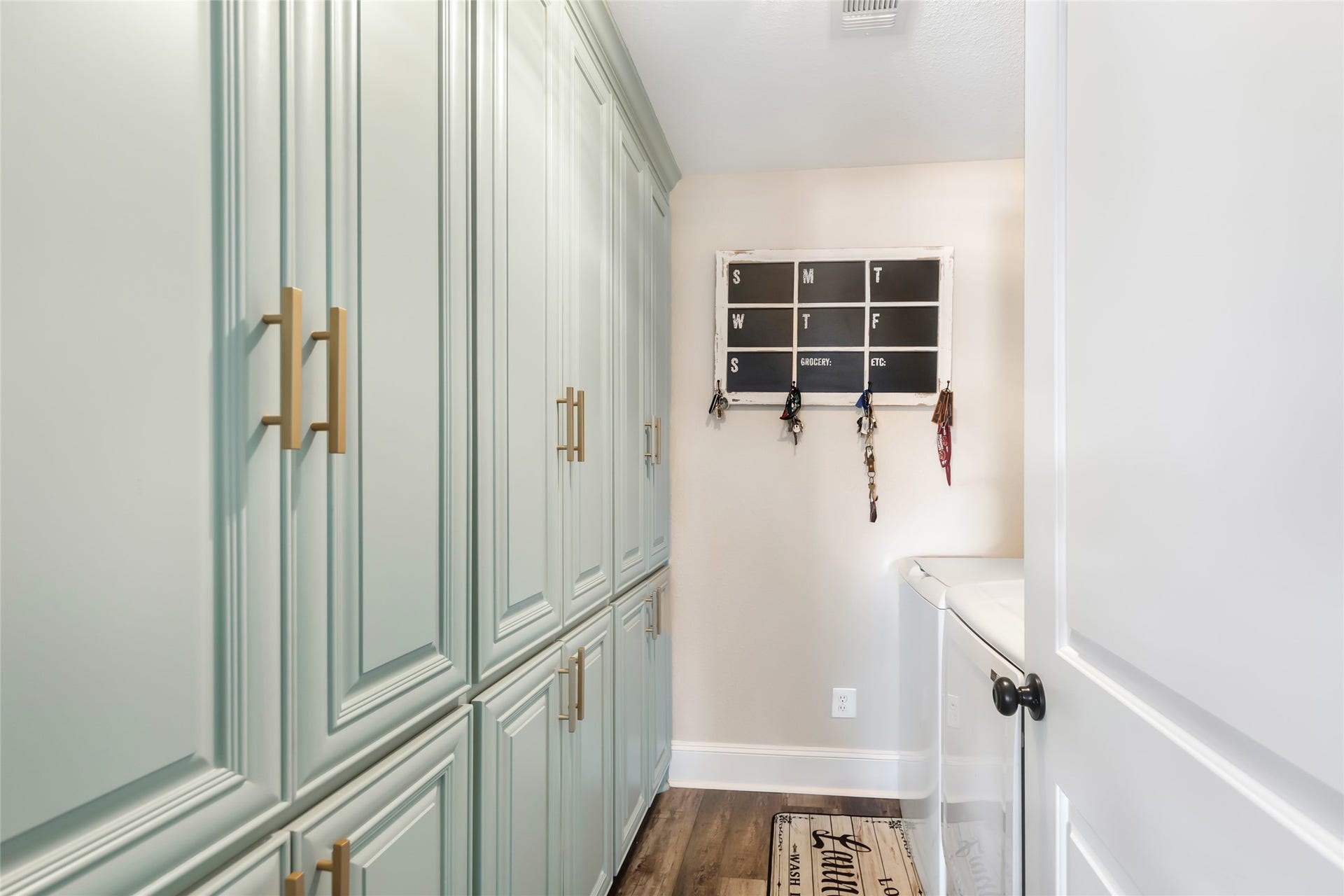 25107 Goodson Road, Splendora, TX 77372 Sleek laundry room featuring abundant cabinet storage, a convenient wall organizer for keys, and a modern washer and dryer setup.