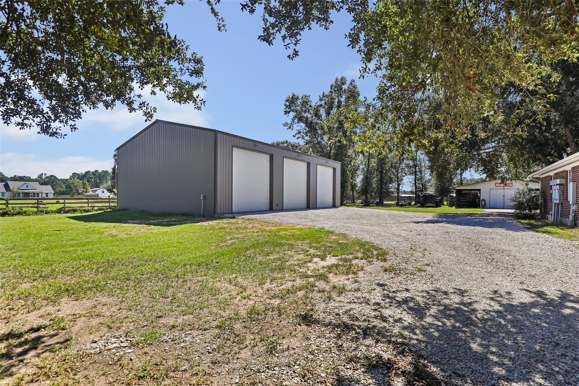 25107 Goodson Road, Splendora, TX 77372 Spacious metal storage building with large roll-up doors, set on a well-maintained gravel driveway, perfect for vehicle storage or a workshop.