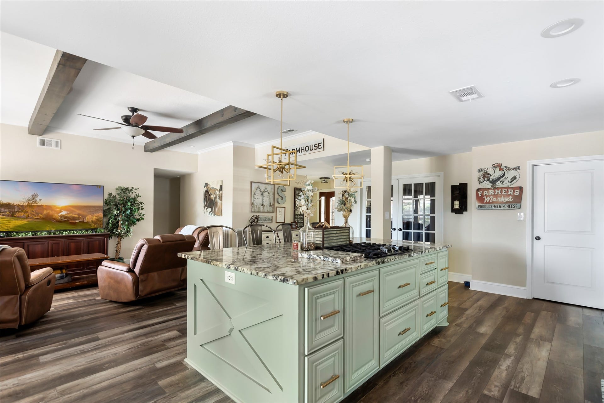 25107 Goodson Road, Splendora, TX 77372 Spacious open-concept kitchen and living area featuring a large island with a granite countertop, modern appliances, and cozy seating with a view of the entertainment space. Wood beams and elegant lighting add charm and warmth.