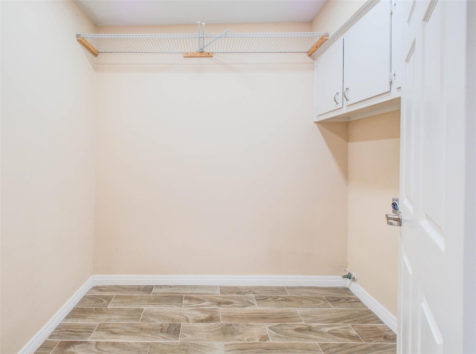 13526 Sherwood Street, Sugar Land, TX 77498 This photo shows a utility room with light walls and wood-look flooring. It features a wire shelf for storage and upper cabinets for additional space.