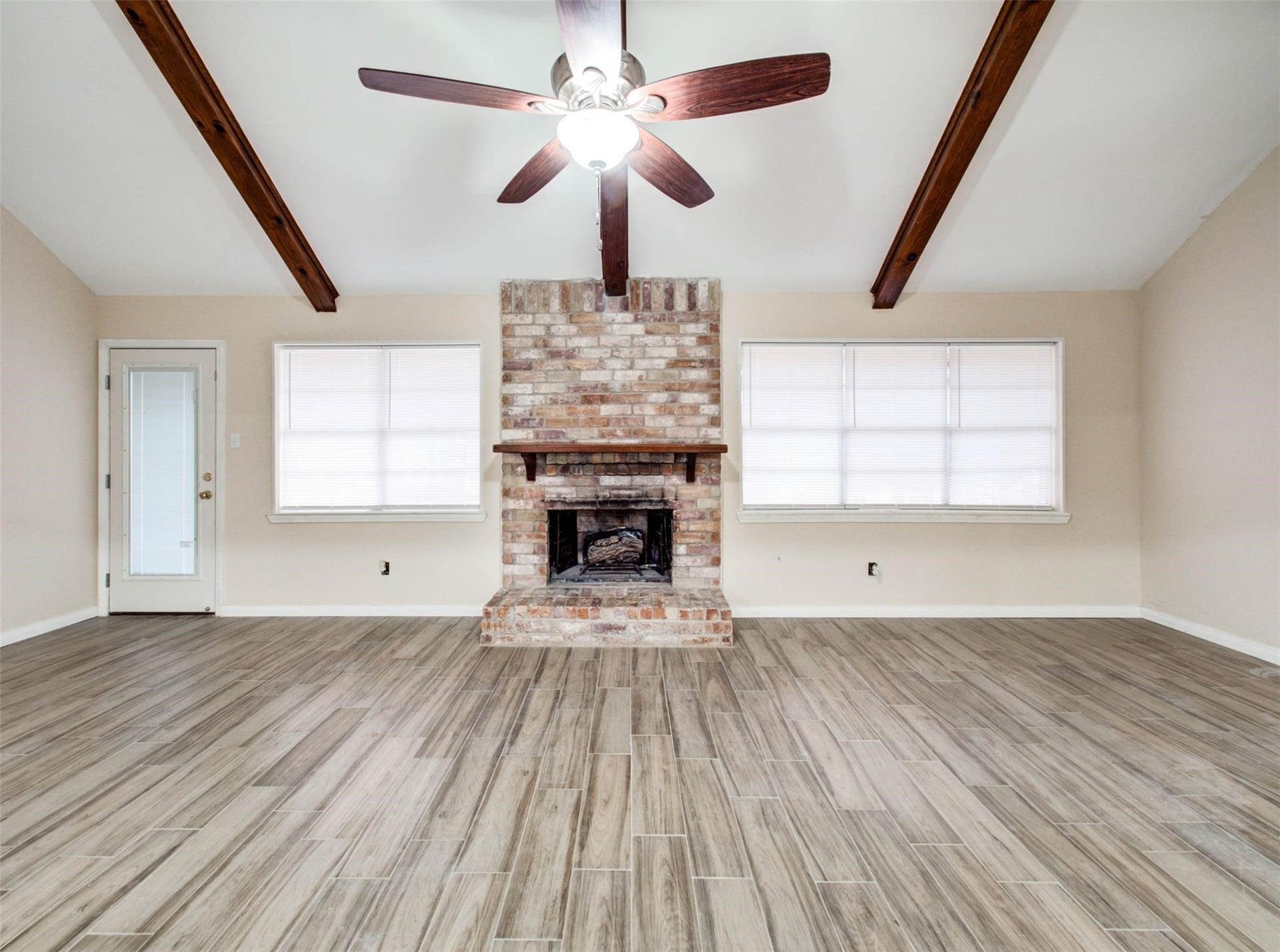 13526 Sherwood Street, Sugar Land, TX 77498 This spacious living room features vaulted ceilings with exposed wooden beams, a central brick fireplace, wood-look flooring, and ample natural light from large windows.