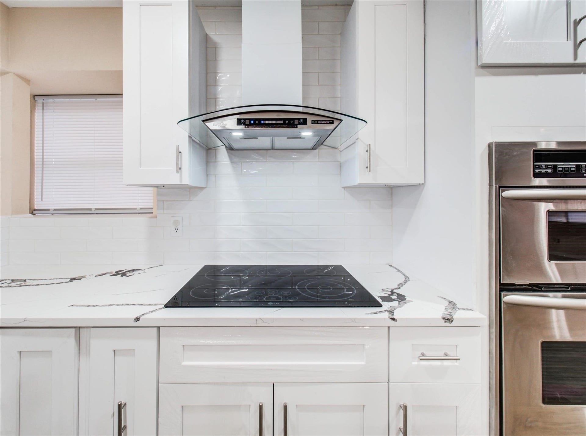13526 Sherwood Street, Sugar Land, TX 77498 Sleek modern kitchen with white cabinetry, a glass range hood, and an electric cooktop. Luxurious granite countertops are paired with stainless steel appliances and a subway tile backsplash for a chic finish.