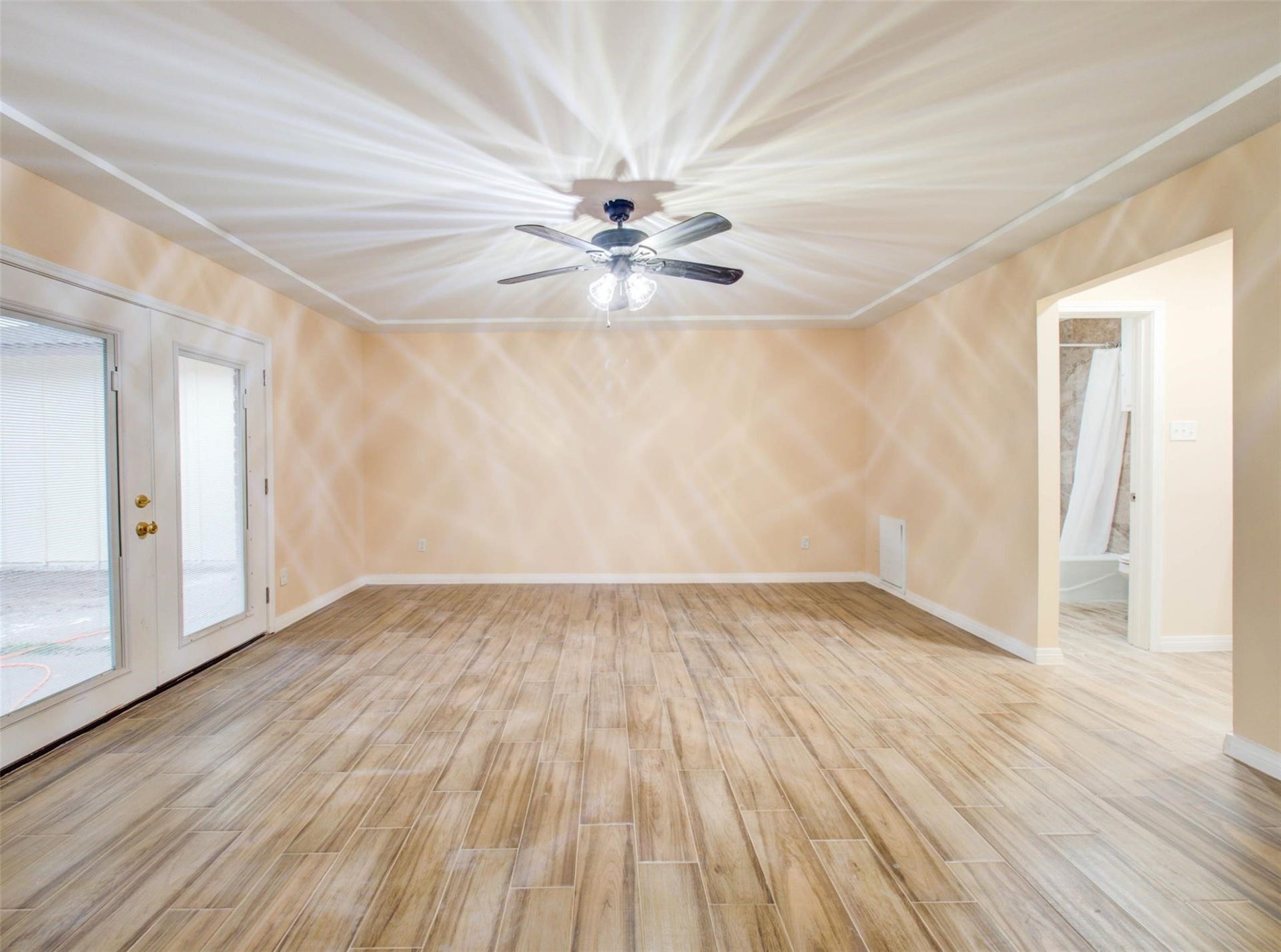 13526 Sherwood Street, Sugar Land, TX 77498 Bright living room with wood-style flooring, ceiling fan, and double doors leading outside. Neutral walls and an open doorway lead to a bathroom, creating a spacious feel.