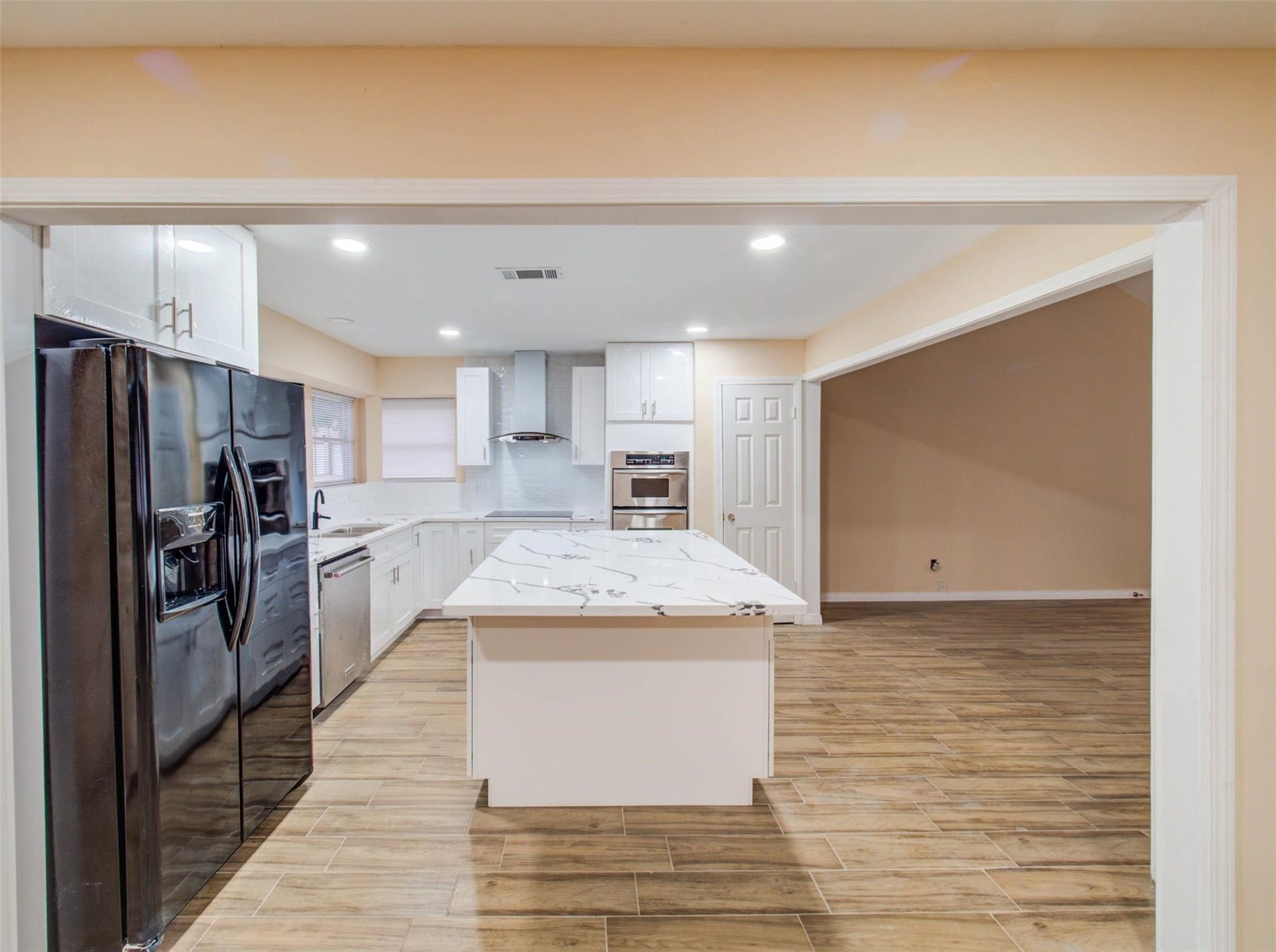 13526 Sherwood Street, Sugar Land, TX 77498 Modern kitchen with sleek black appliances and a central island featuring a granite countertop. The space is open and bright, with wood-look flooring and white cabinetry.